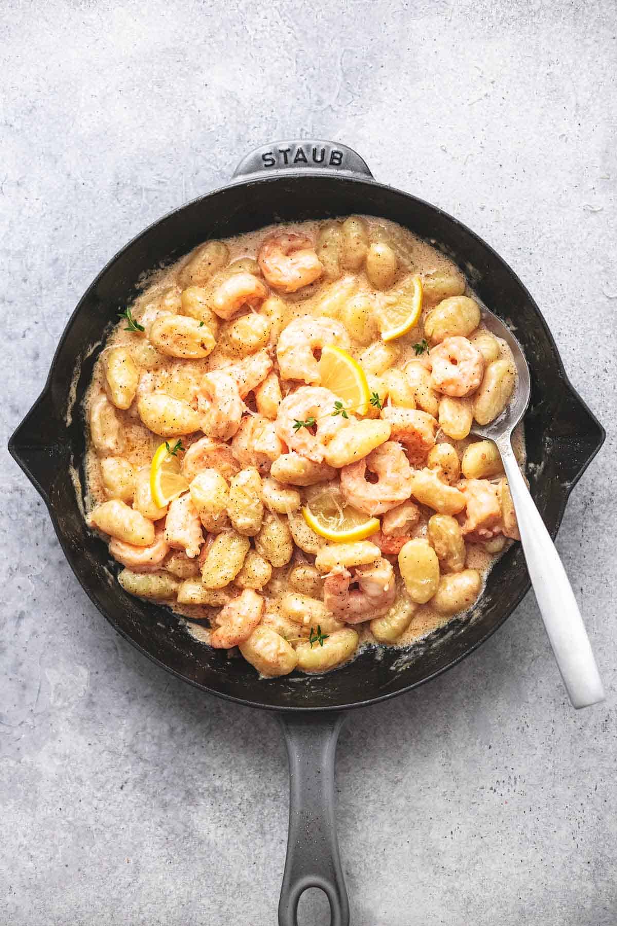 top view of creamy lemon garlic shrimp and gnocchi with a serving spoon in a skillet.