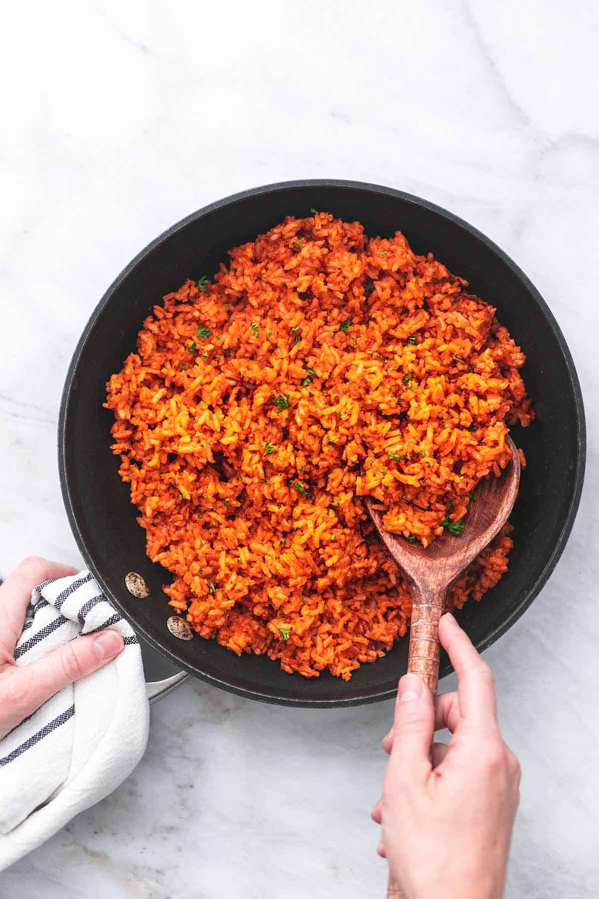 top view of Mexican rice in a skillet with a hand holding the handle and a serving spoon in the skillet.