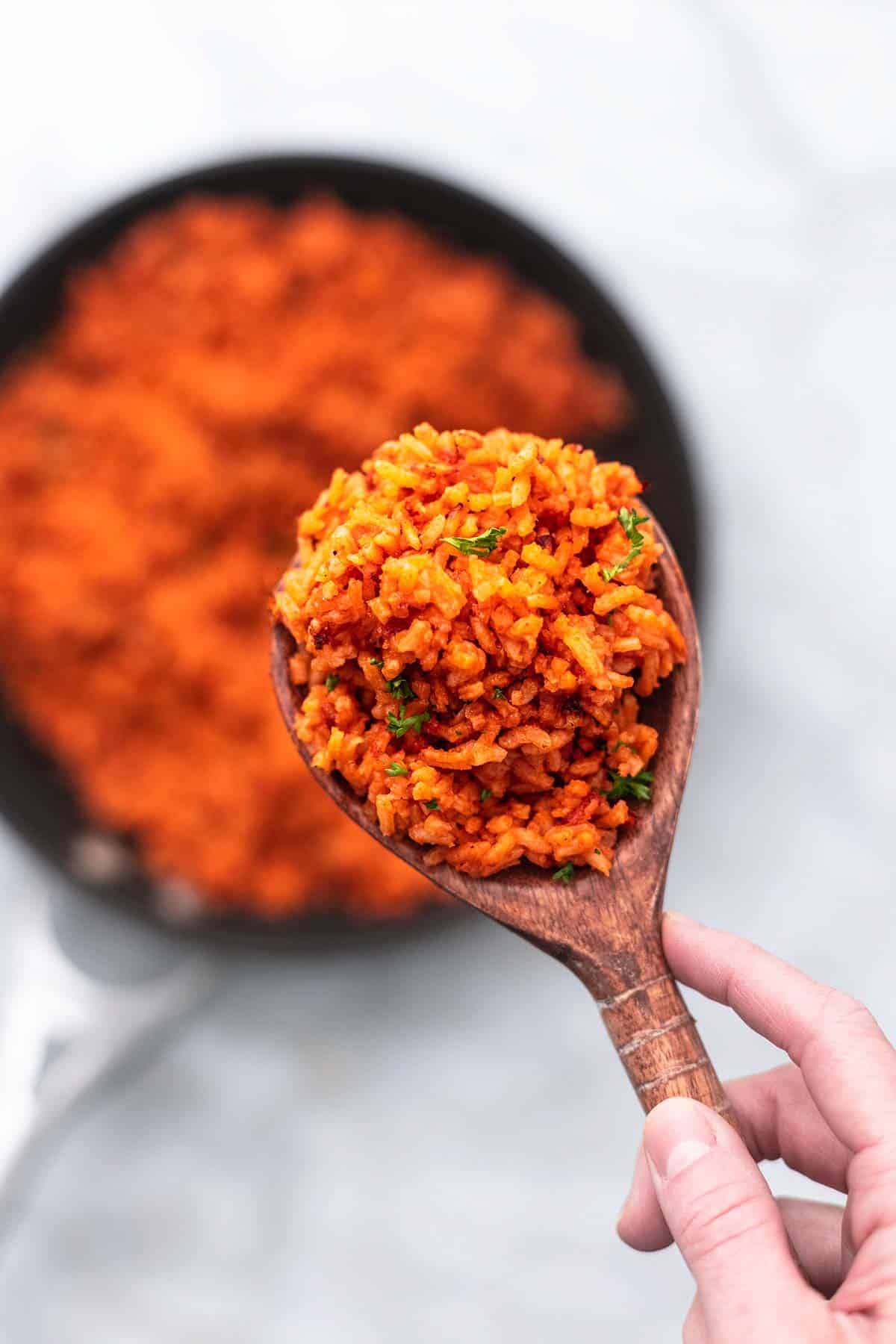 top view of a hand holding up Mexican rice in a serving spoon above a skillet of rice.