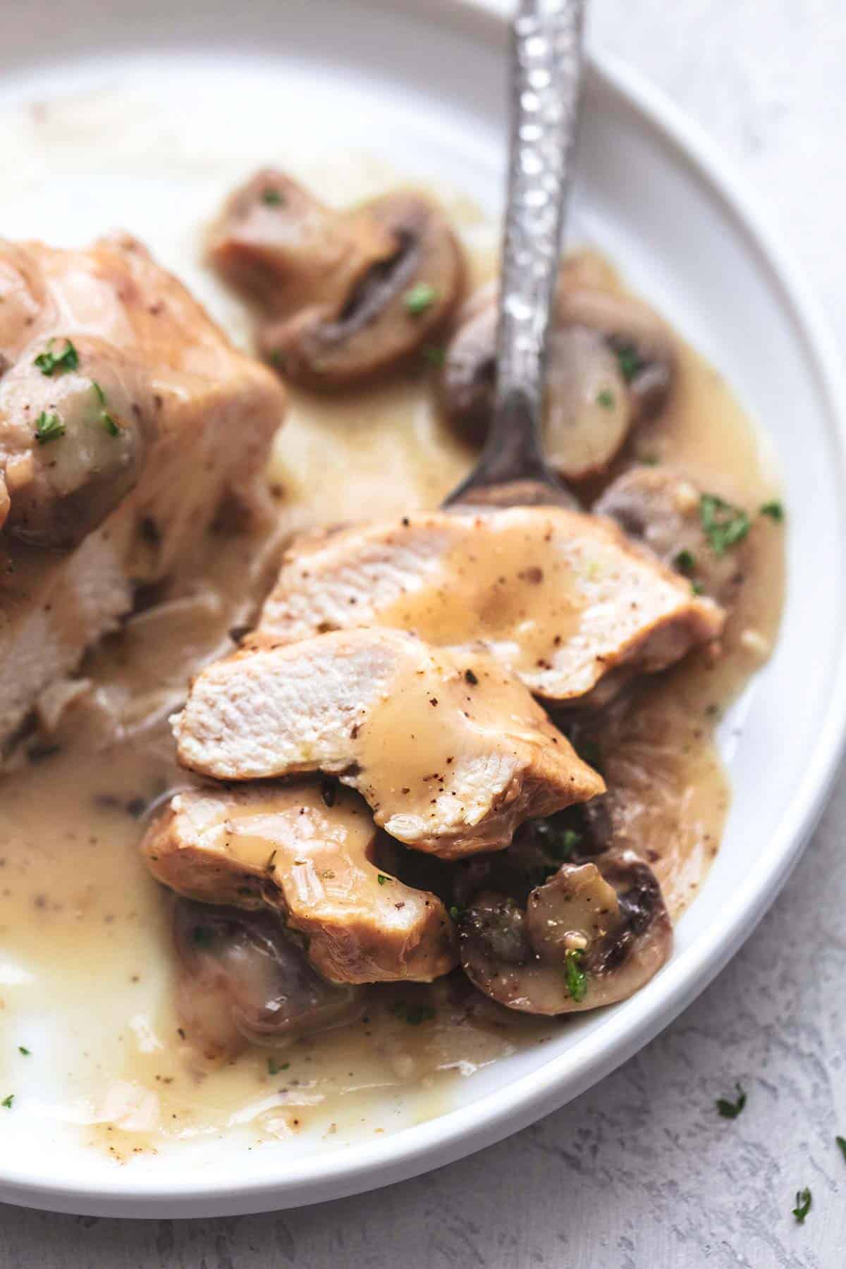sliced chicken with gravy and mushrooms with a fork on a white plate close up