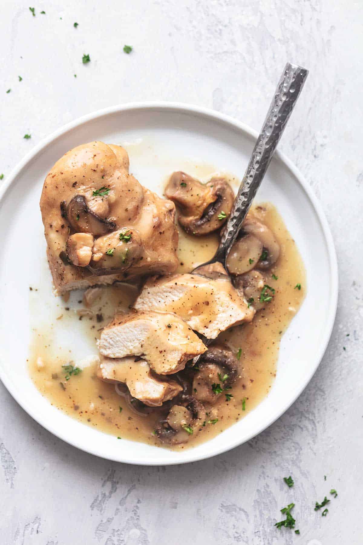 sliced chicken with gravy and mushrooms with a fork on a white plate