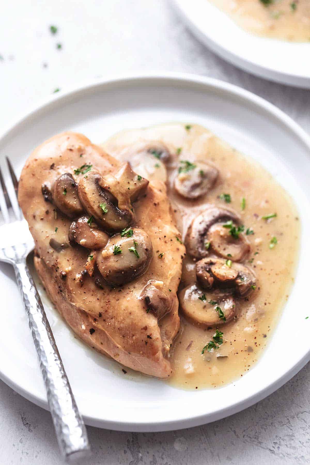 chicken with gravy and mushrooms on a white plate with a fork close up