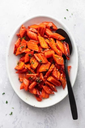 cooked carrots on a serving platter with a spoon overhead