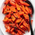 cooked carrots on a serving platter with a spoon overhead
