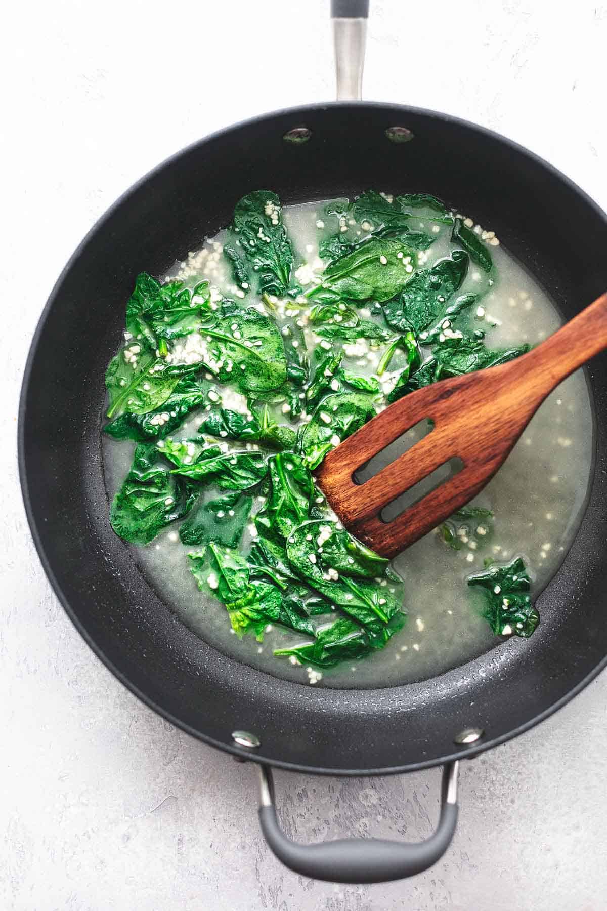 top view of sautéed spinach with a serving spoon in a skillet.