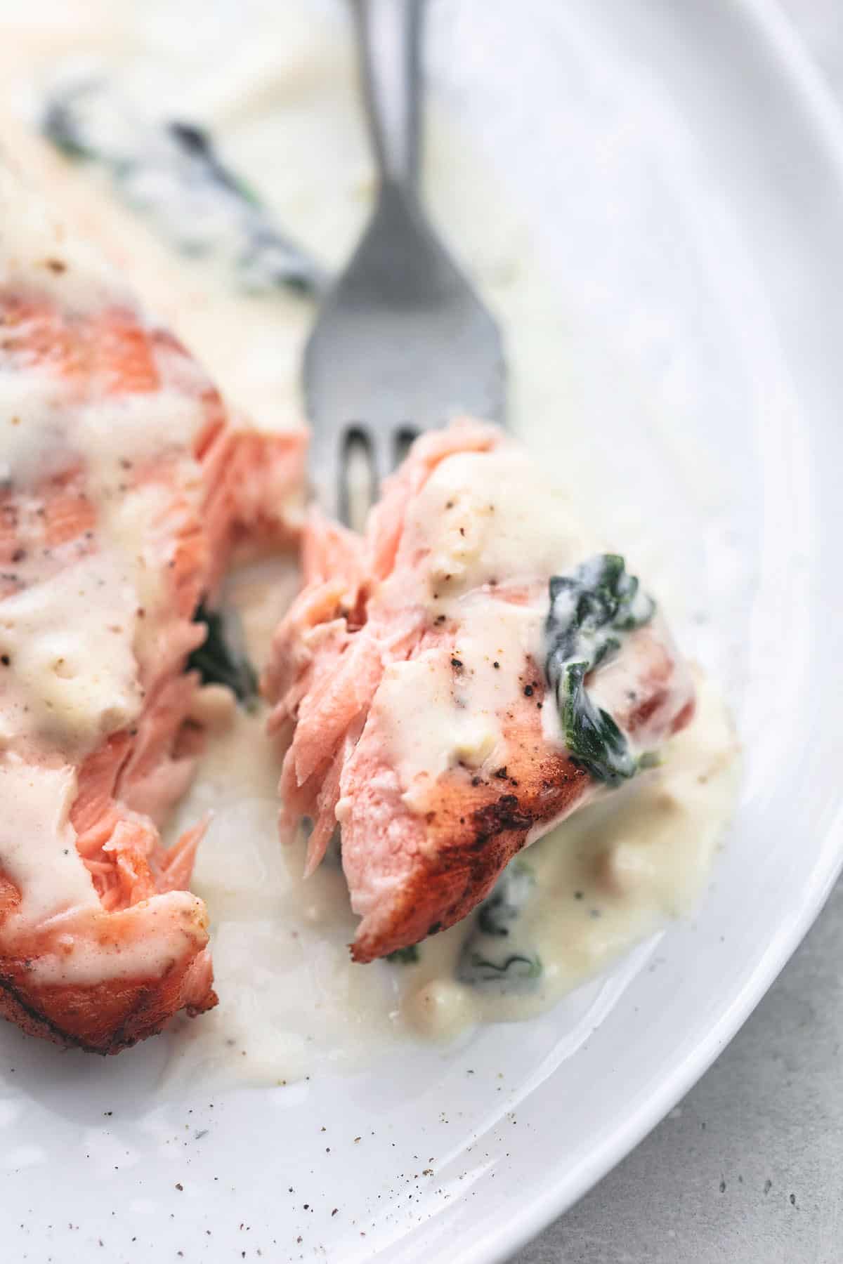 up close bite of salmon with creamy spinach sauce on a fork