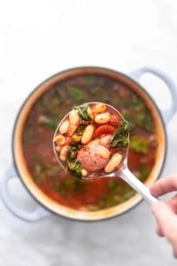 white bean and sausage soup in a ladle above a soup pot
