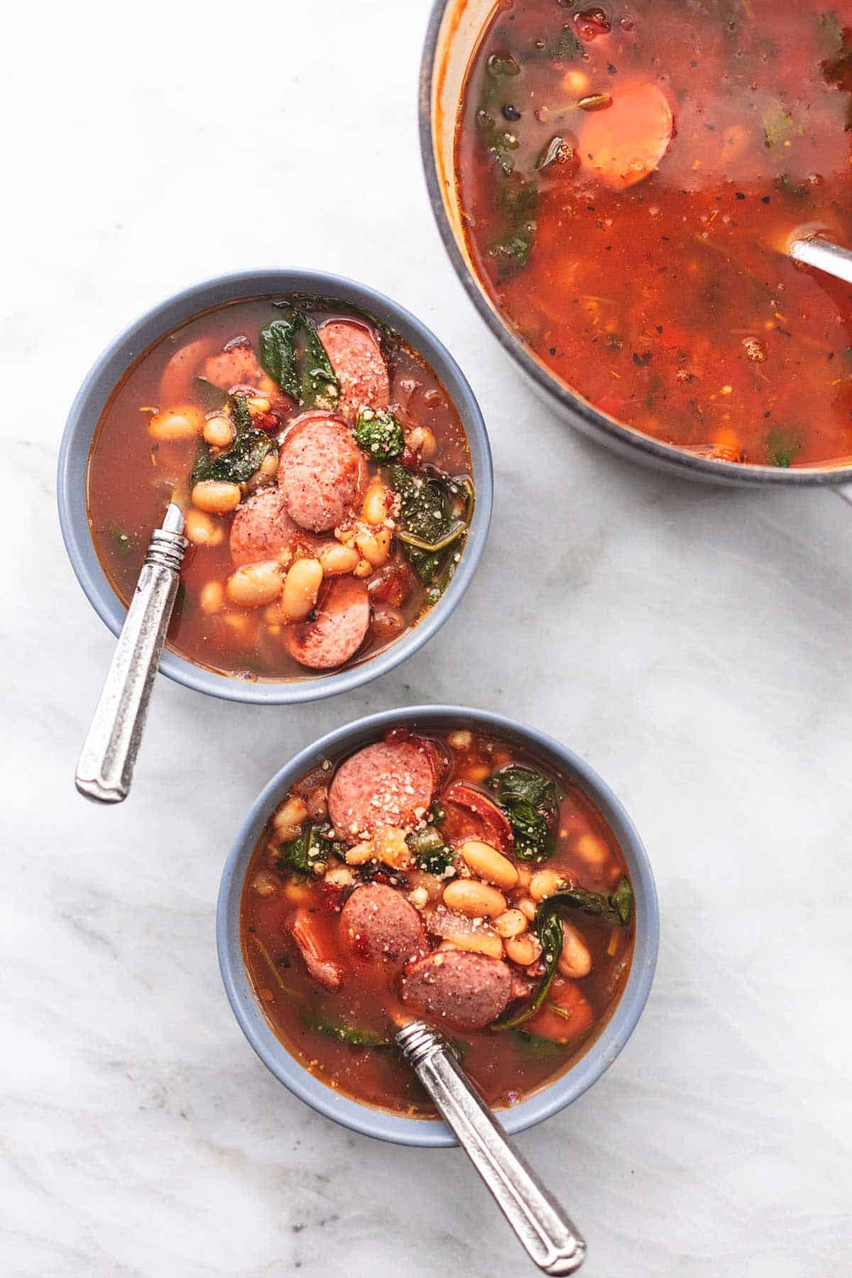 two bowls and a soup pot with sausage white bean soup
