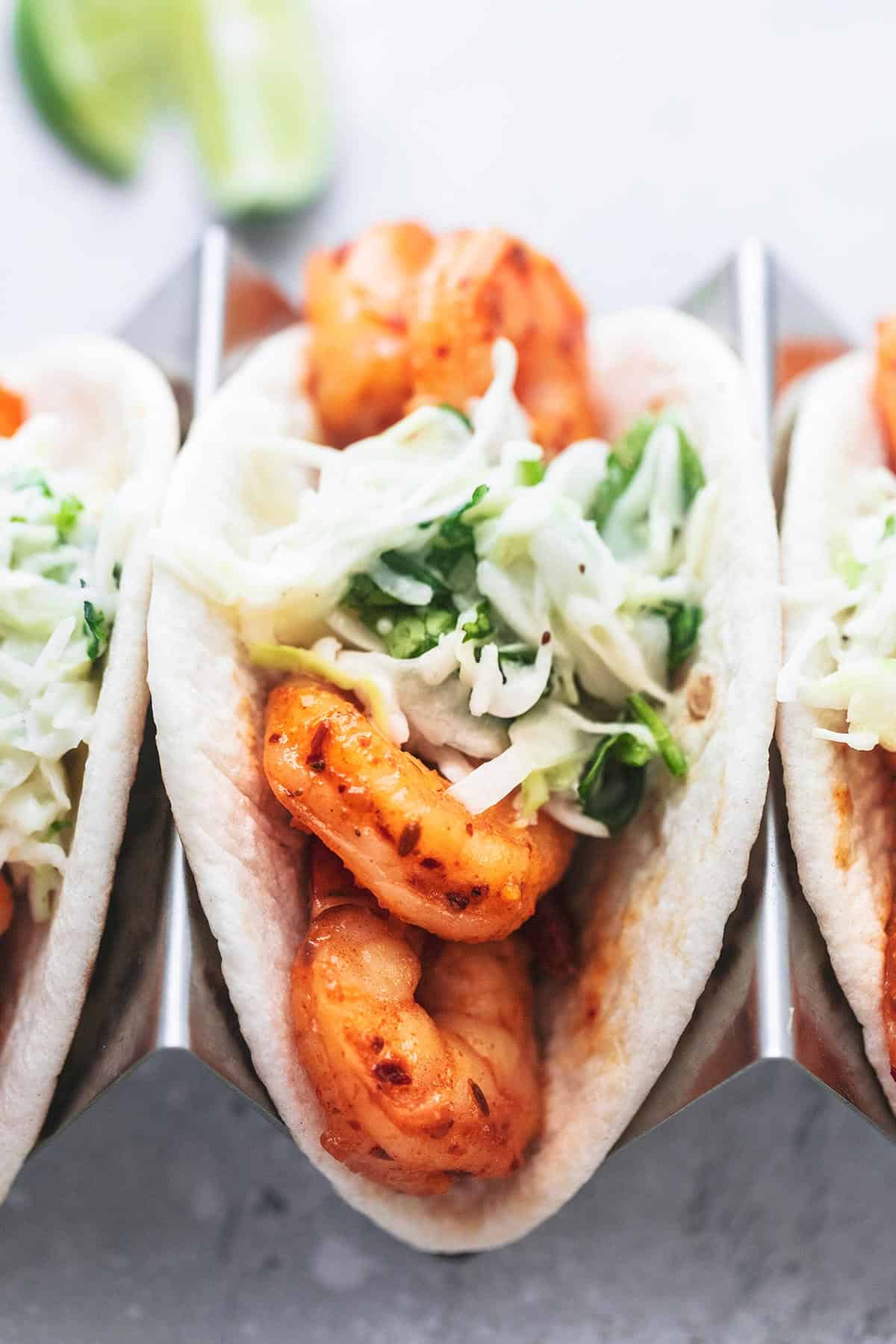 close up of a shrimp taco with slaw in a taco holder with more tacos on the sides.