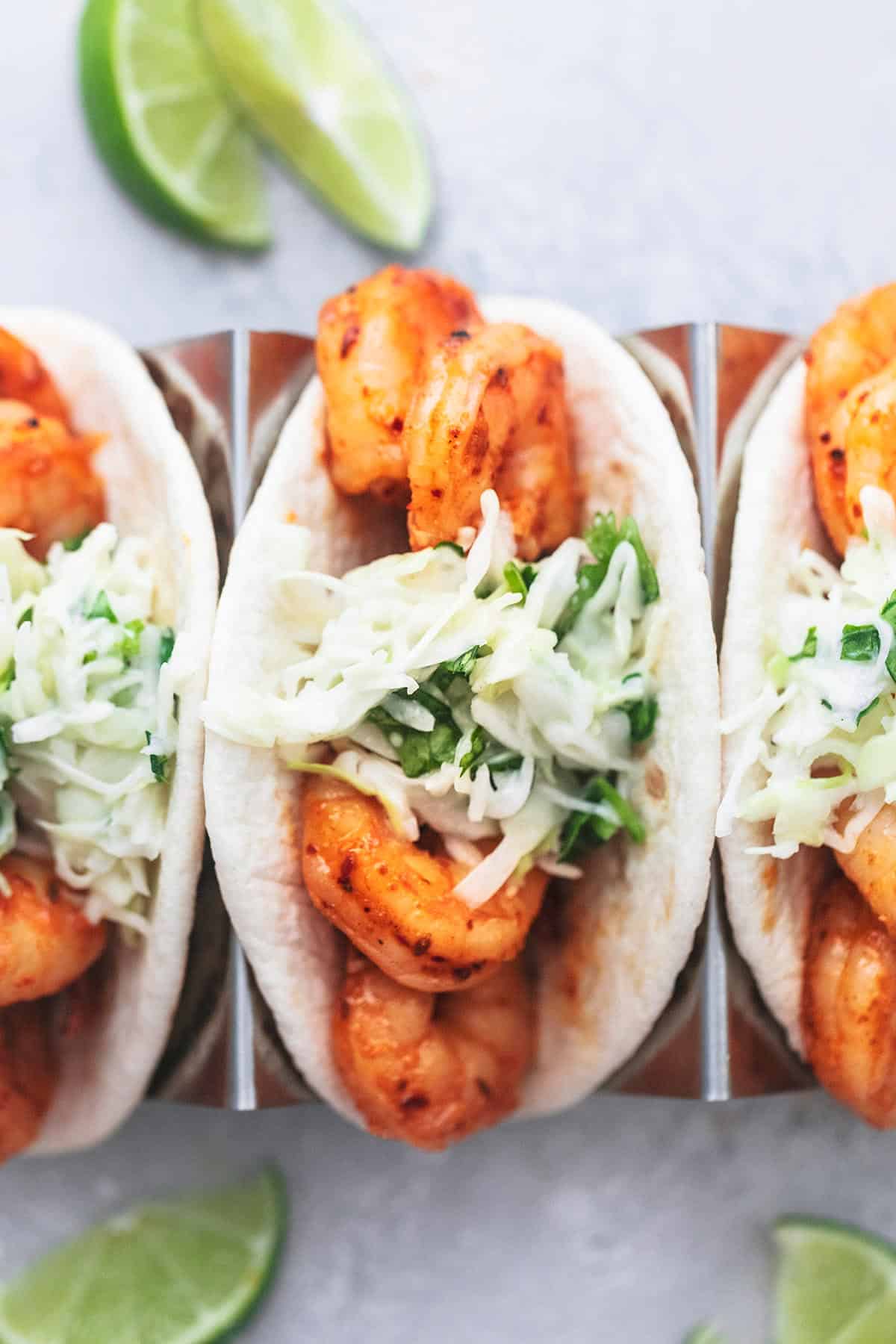 close up top view of shrimp tacos with slaw in taco holders with lime slices on the side.