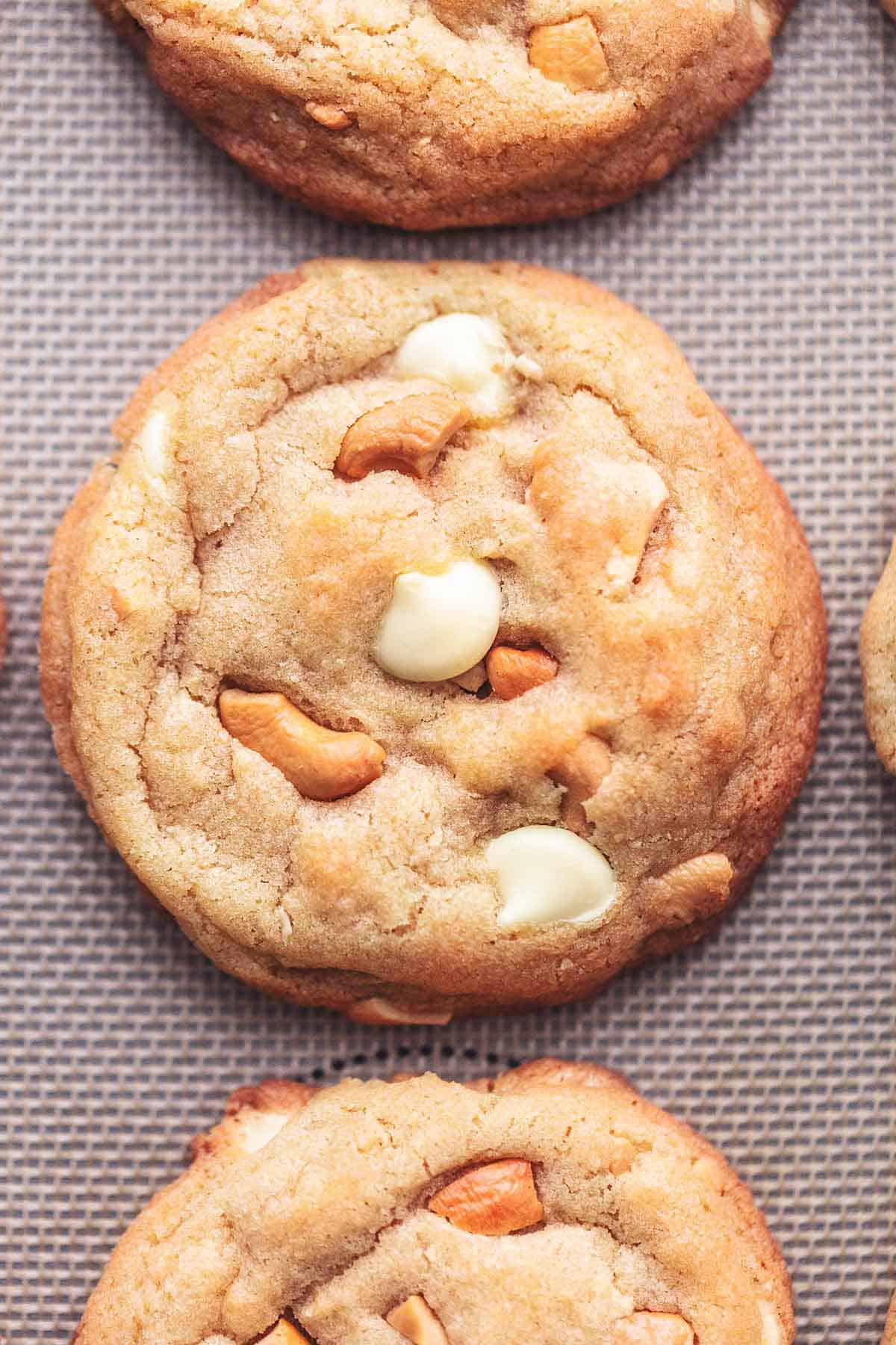 close up top view of a chewy white chocolate cashew cookie with more cookies on the side.