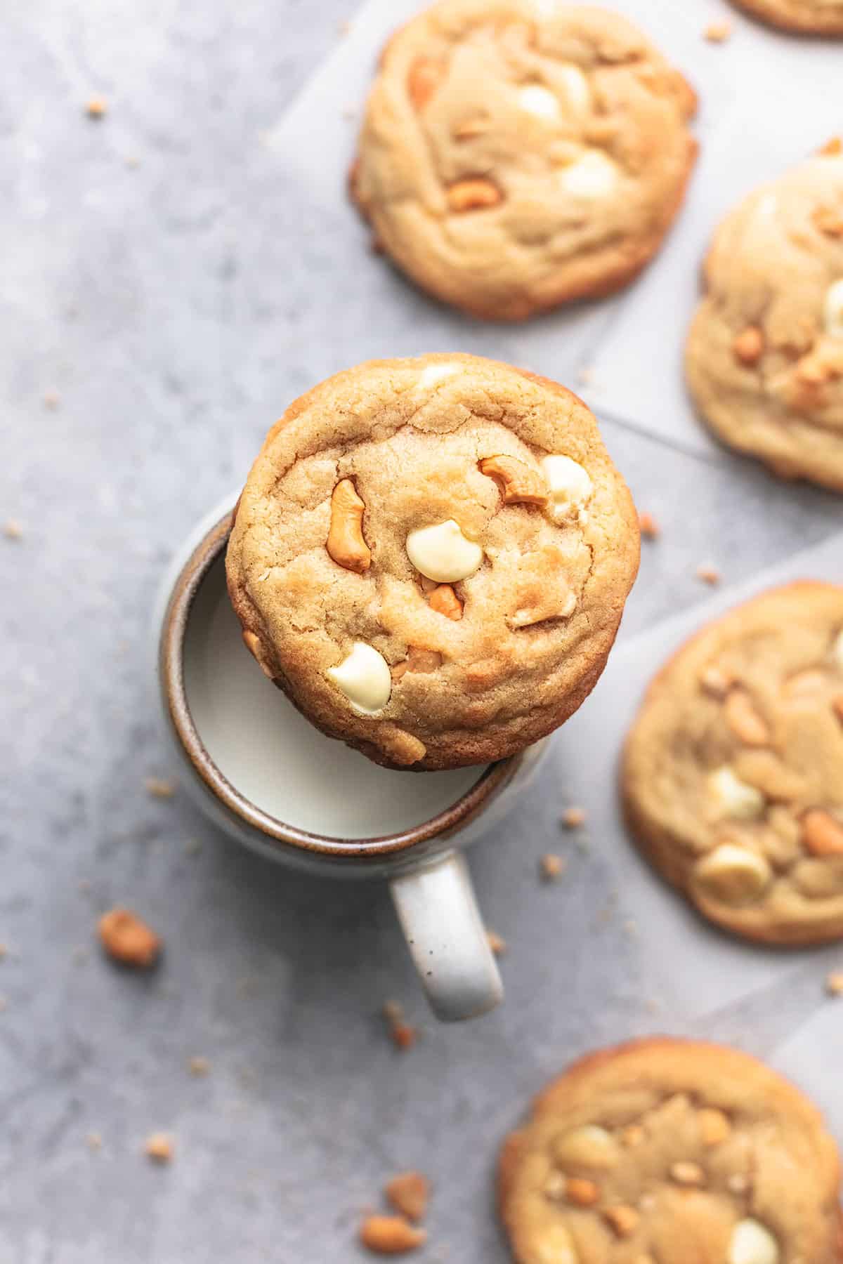 top view of a chewy white chocolate cashew cookie on a mug of milk with more cookies on the side.