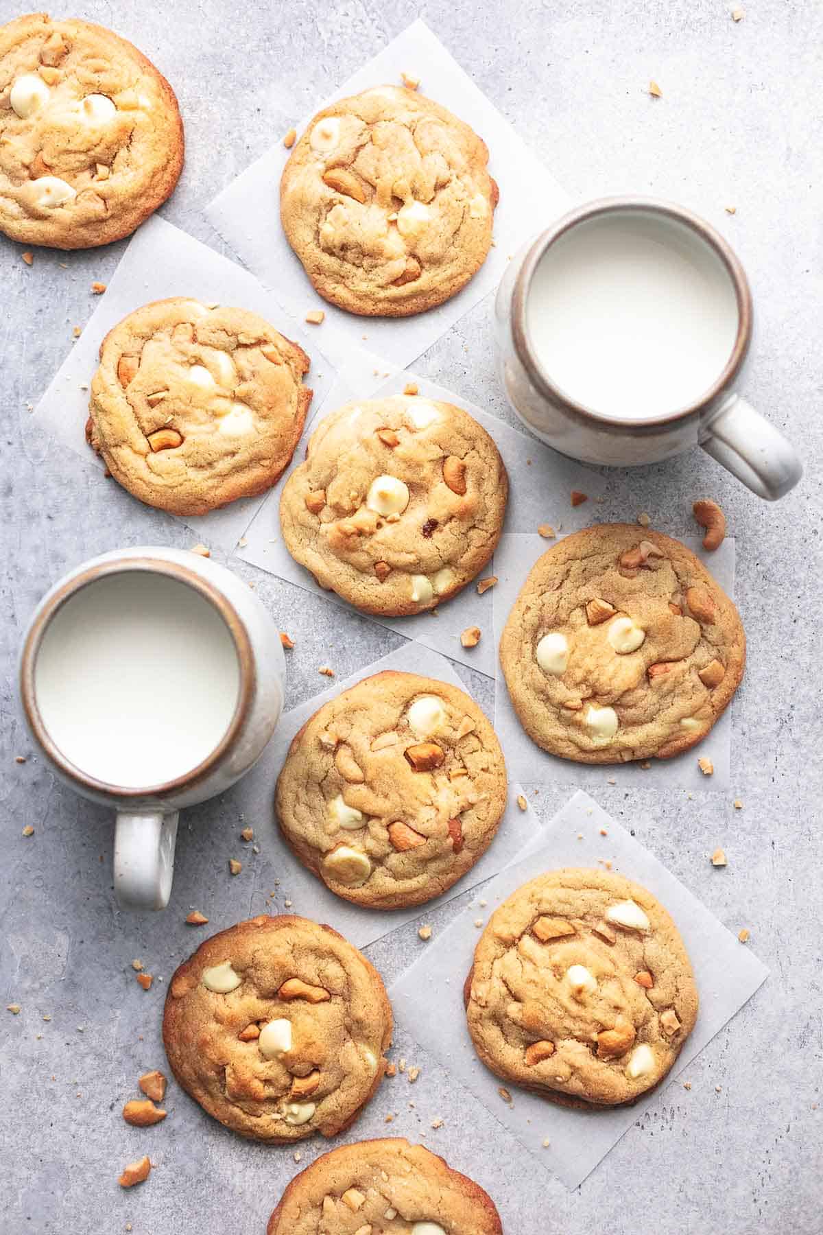 top view of chewy white chocolate cashew cookies with two mugs of milk on the side.