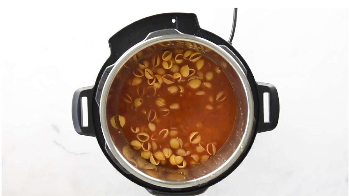 Cooked pasta shells in red sauce in pot.