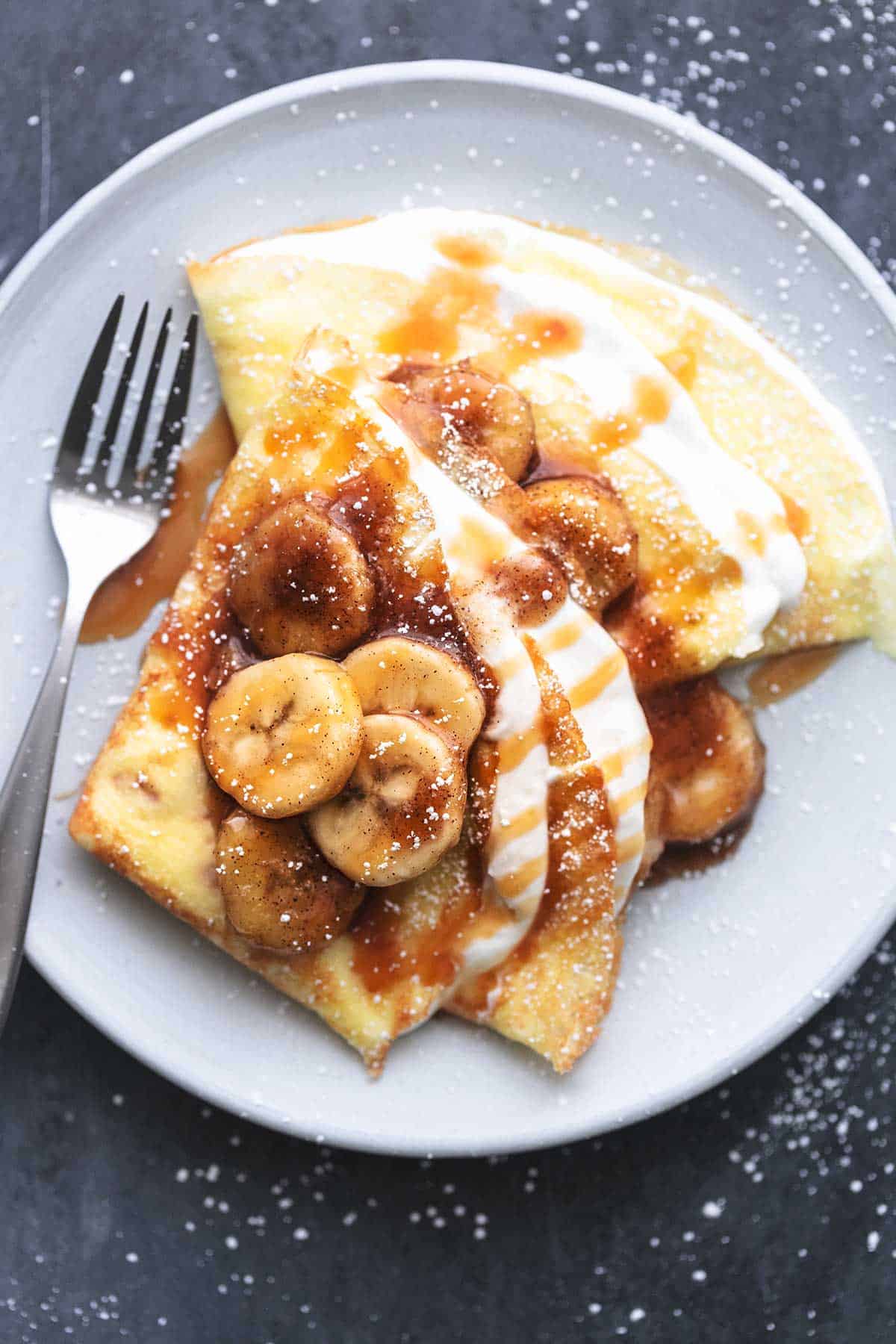 top view of crepes with banana crepe filling in them with a fork on a plate.