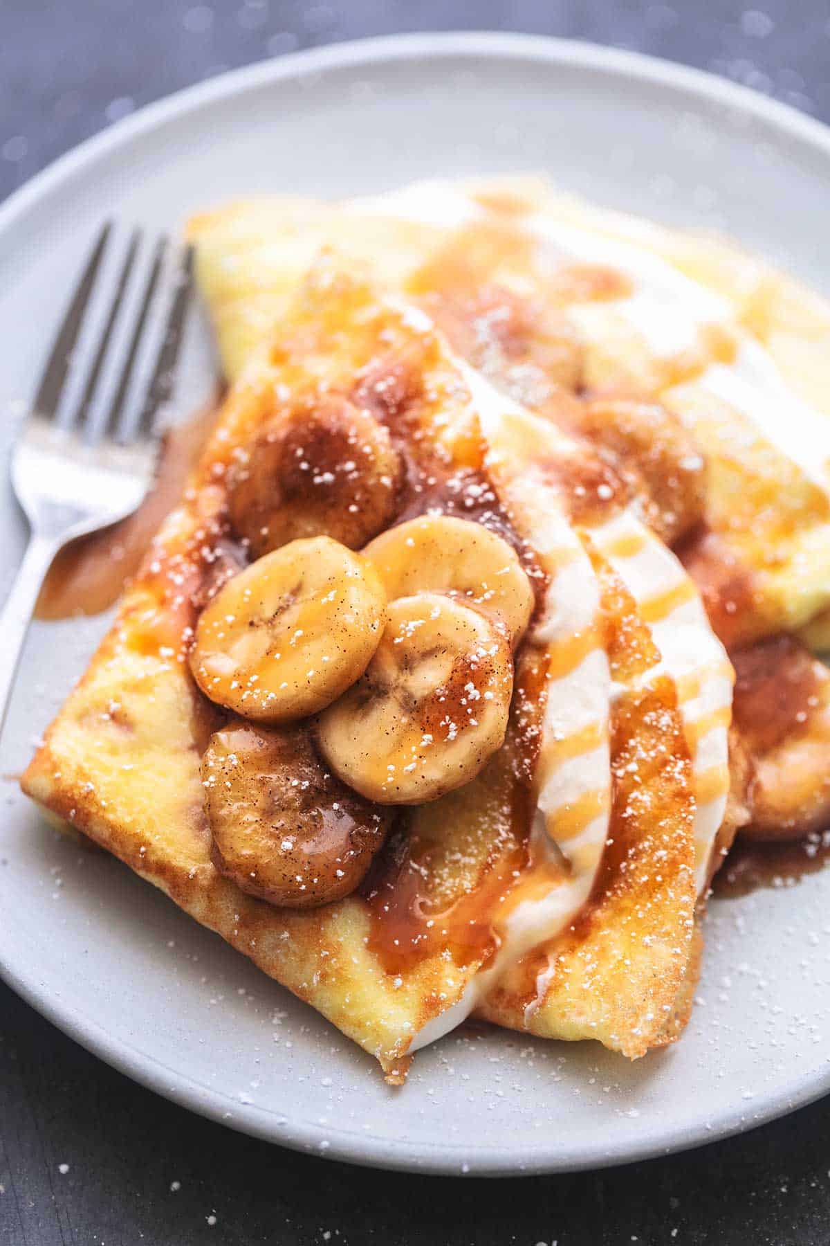 close up of crepes with banana crepe filling and a fork on a plate.