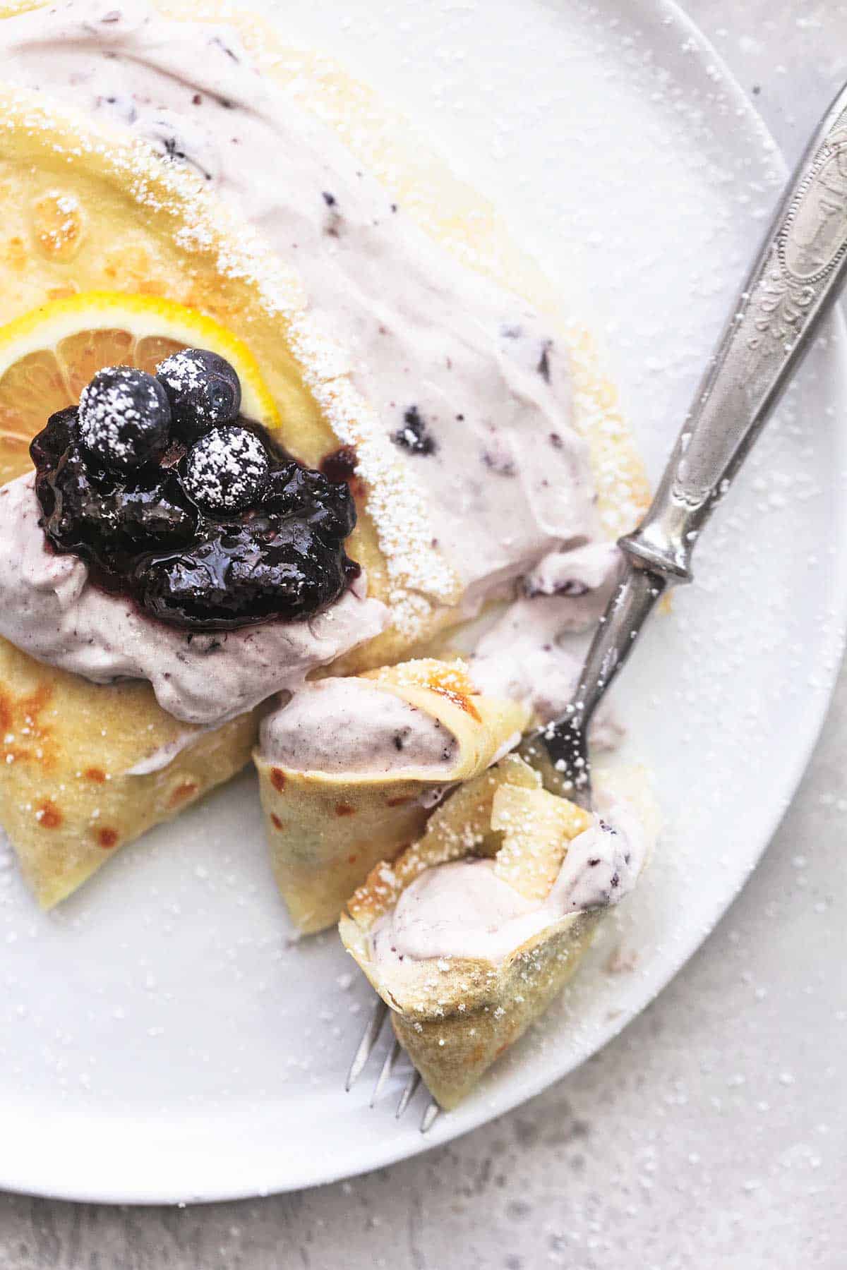 close up top view of a crepe with blueberry filling with a bite on a fork all on a plate.