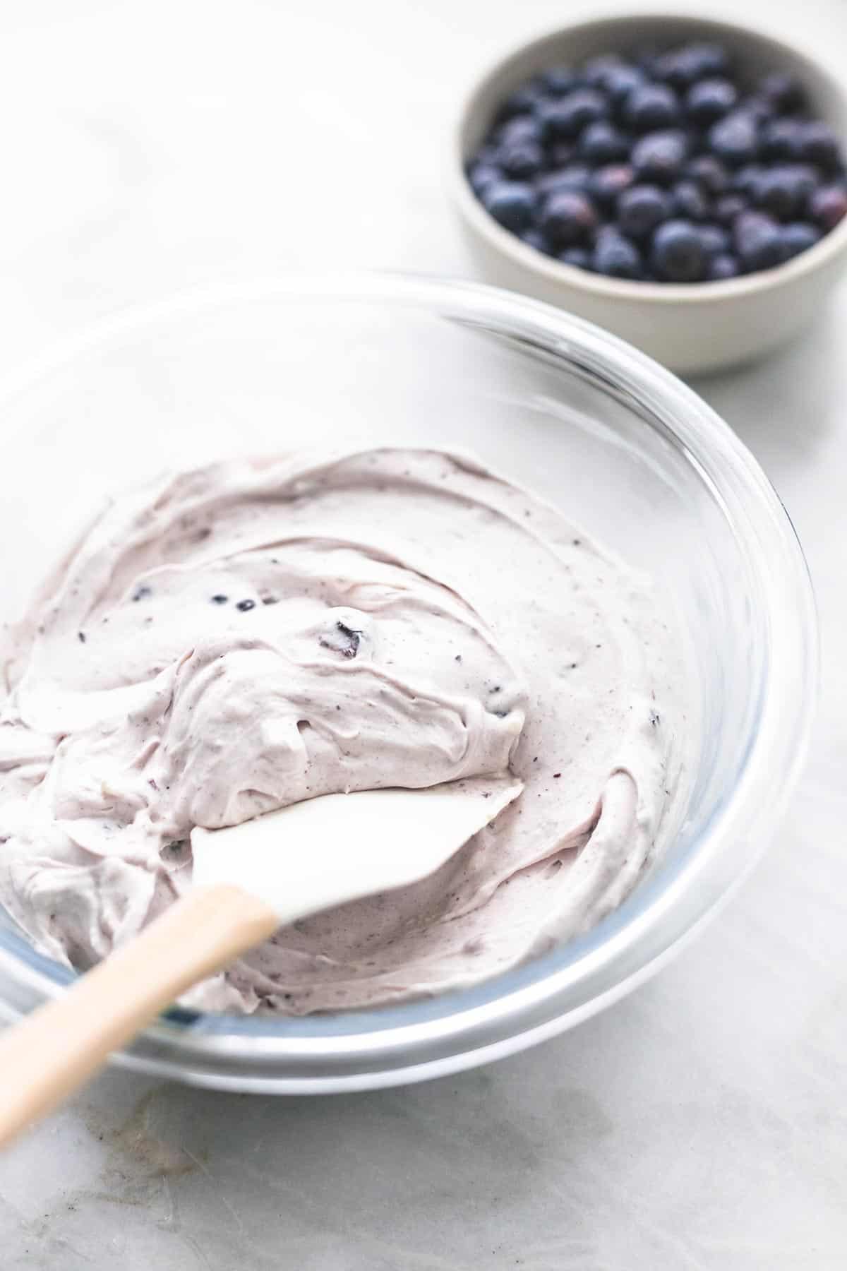 blueberry crepe filling in a glass bowl with a spatula with a bowl of blueberries on the side.