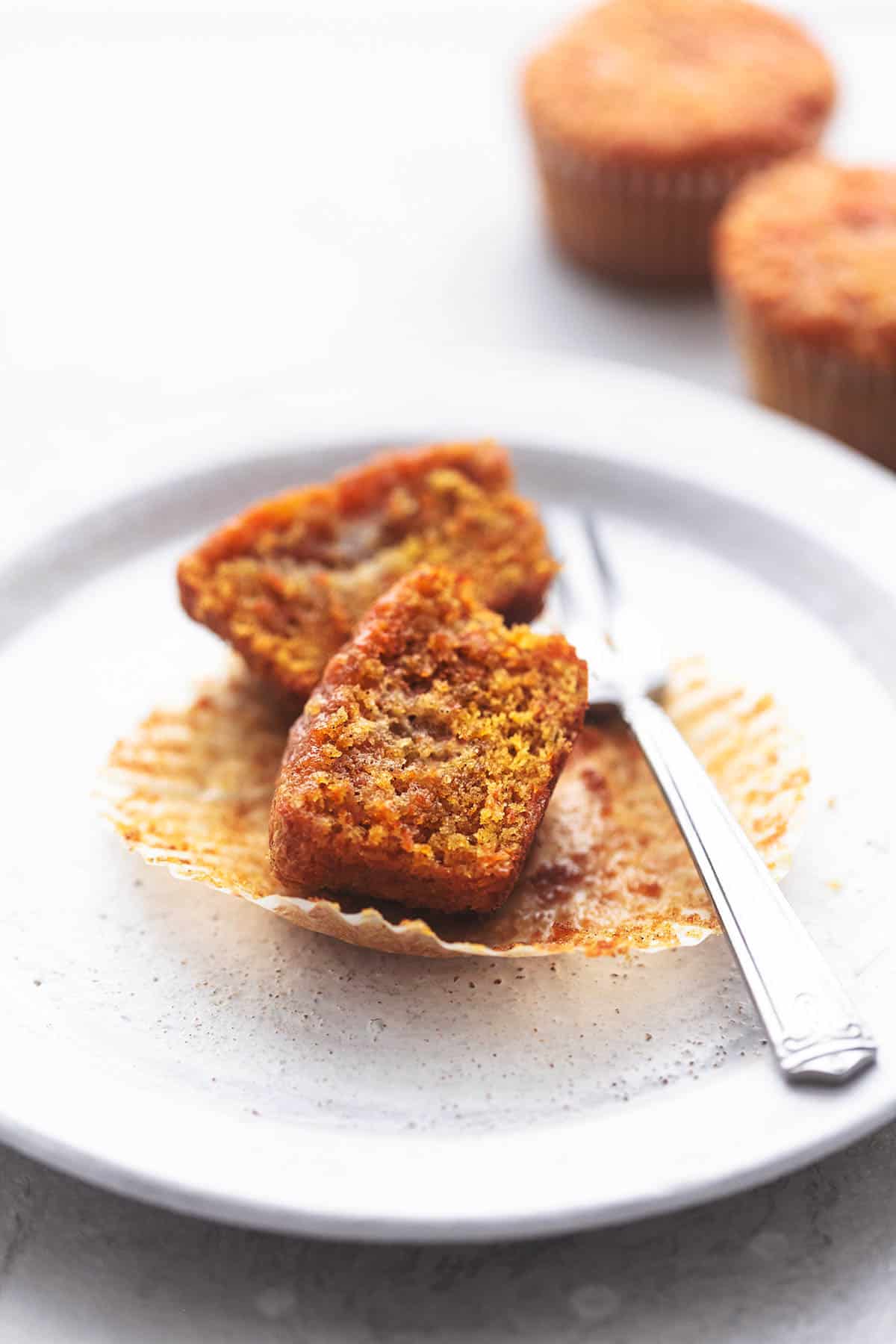 a carrot cake muffin cut in half with a fork on a plate with more muffins on the side.