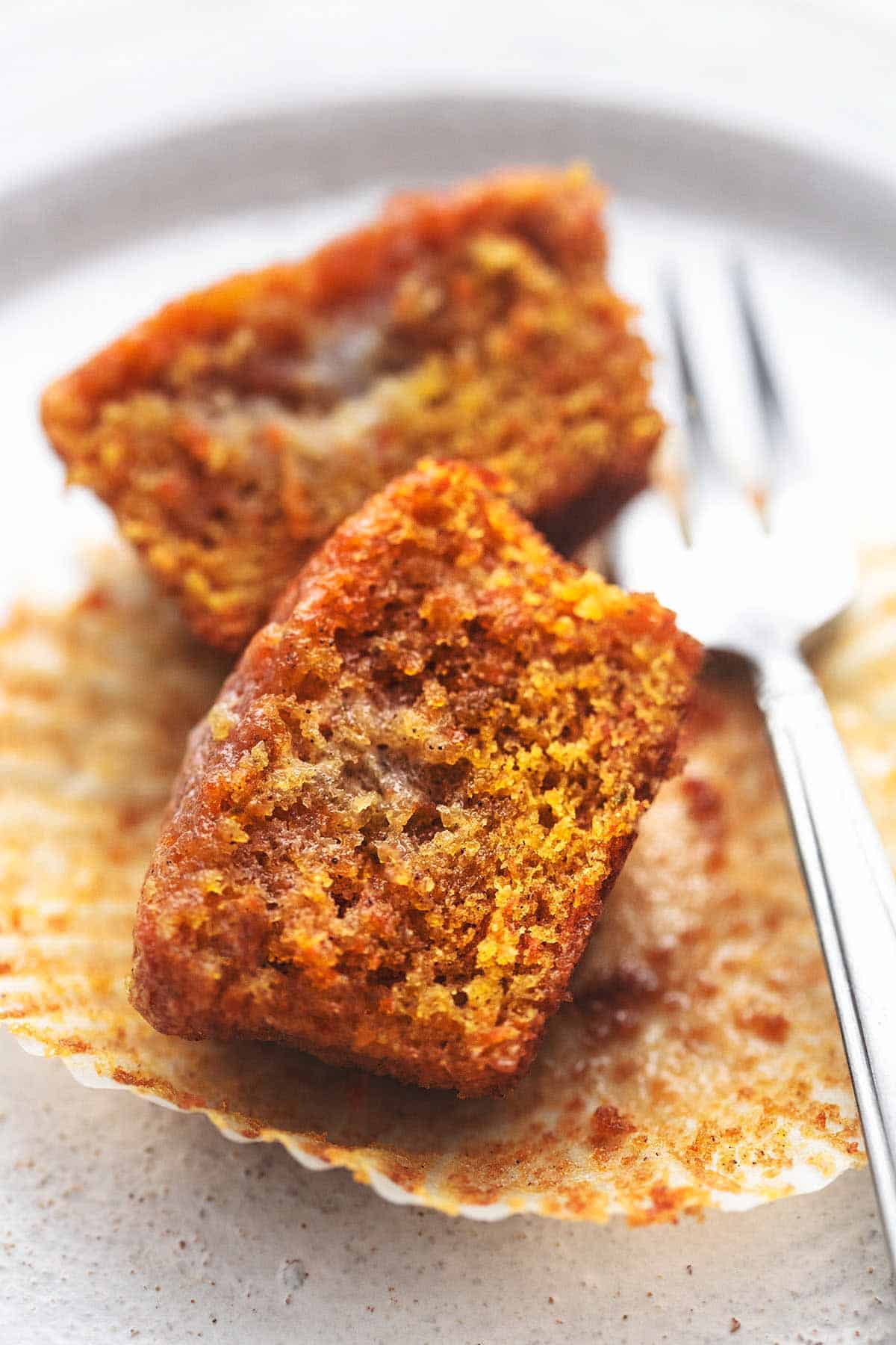 close up of a carrot cake muffin cut in half with a fork on the side on a plate.