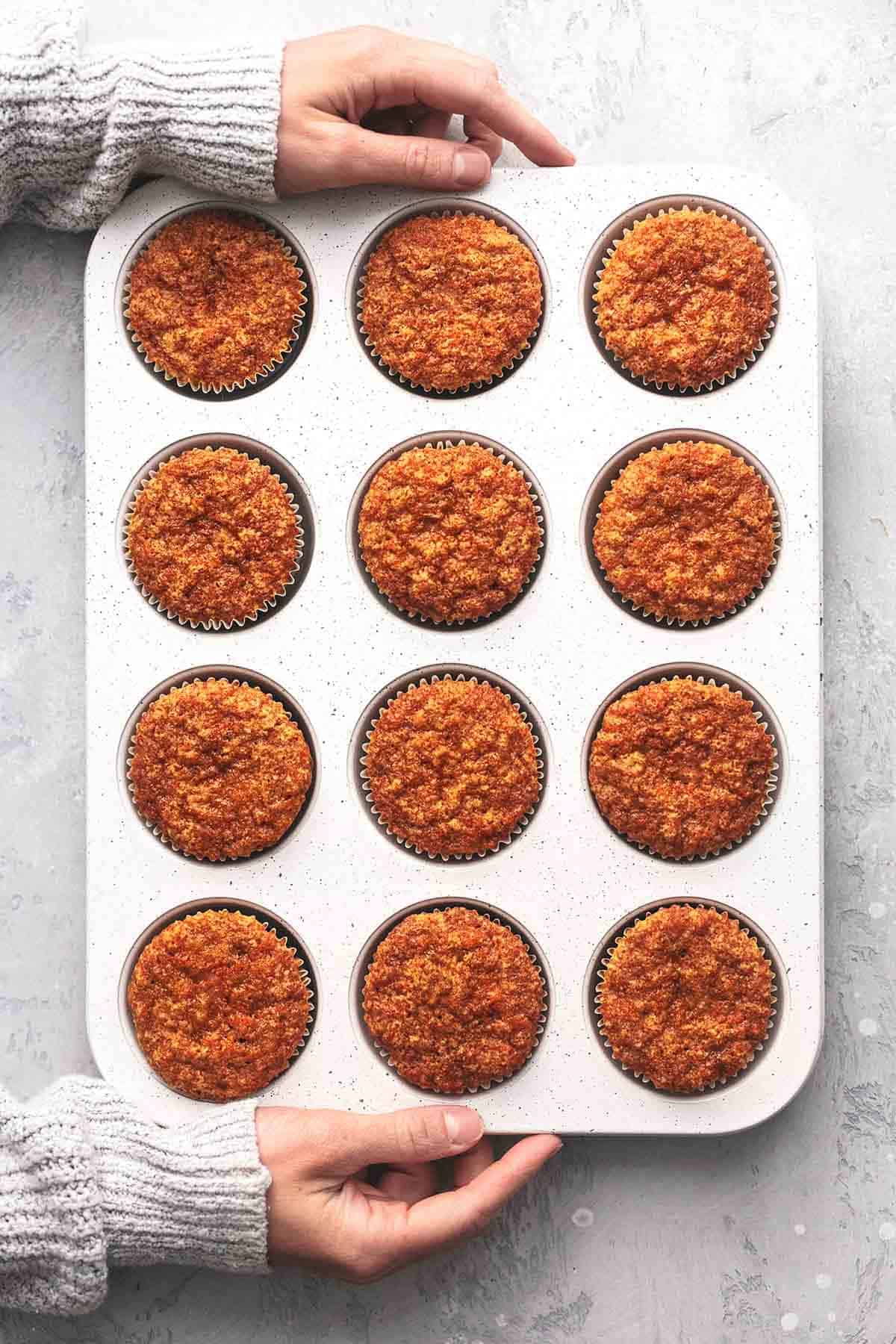 top view of hands holding muffin tin with carrot cake muffins.