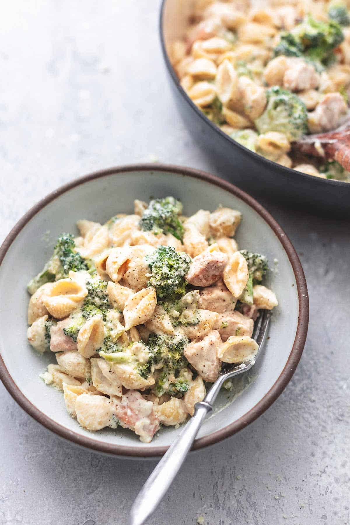 chicken alfredo with broccoli in a bowl with a fork with a skillet of more pasta on the side.