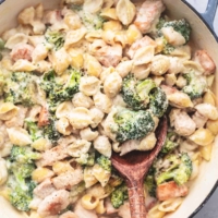 chicken alfredo pasta shells with broccoli and serving spoon in skillet