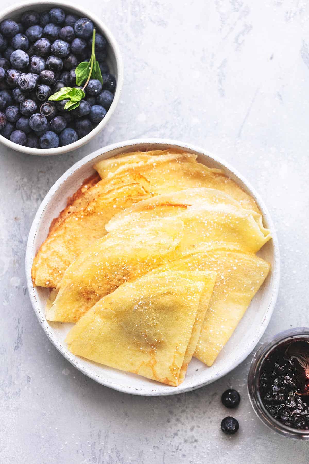 top view of crepes on a plate with blueberries on the side in a bowl.