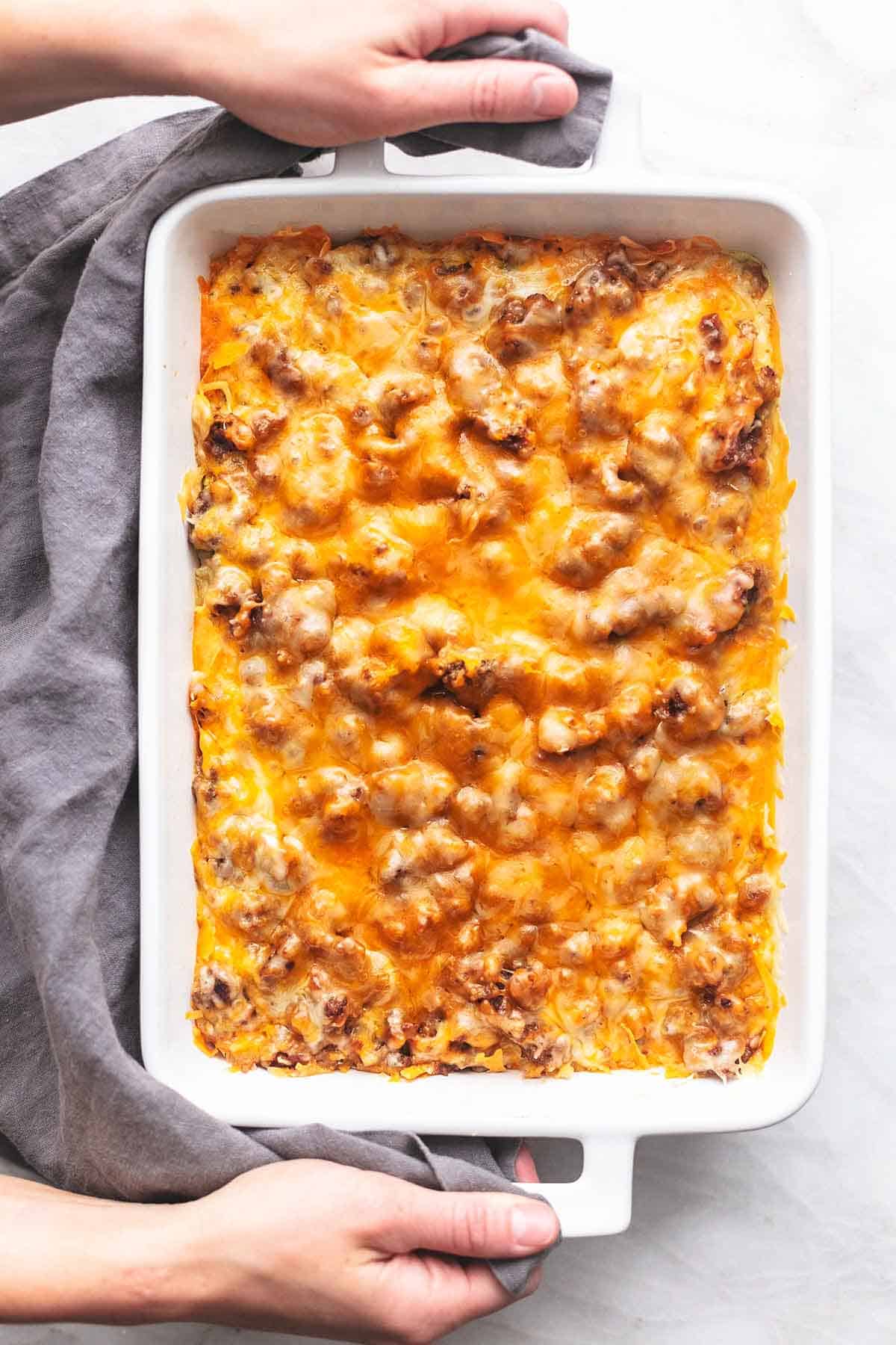 top view of hands holding a baking dish of sausage breakfast casserole.