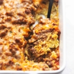 up close egg and hashbrown and sausage breakfast casserole in a white baking dish with a serving spoon