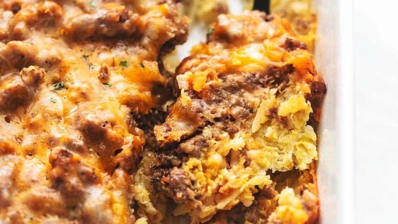 up close egg and hashbrown and sausage breakfast casserole in a white baking dish with a serving spoon
