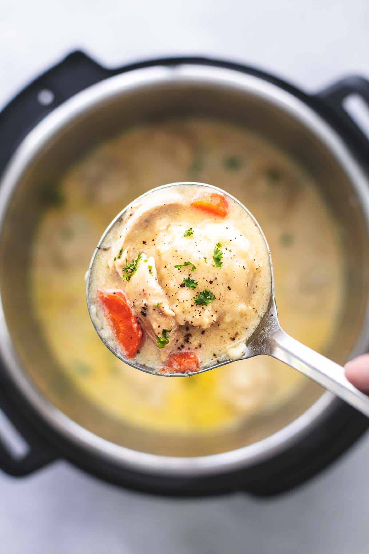 top view of a ladle full of instant pot chicken and dumplings being held above an instant pot of more soup.