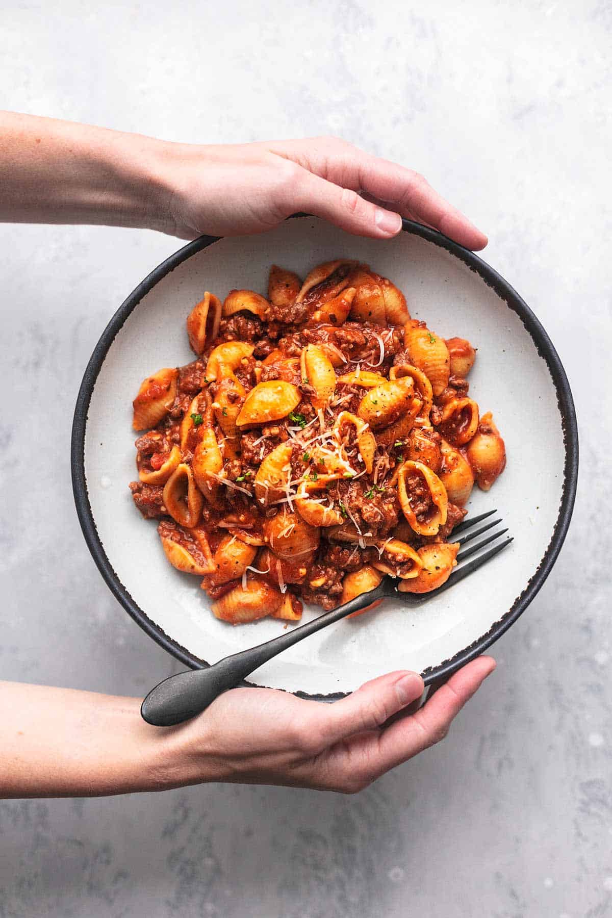 top view of hands holding plate of instant pot ground beef pasta with a fork.