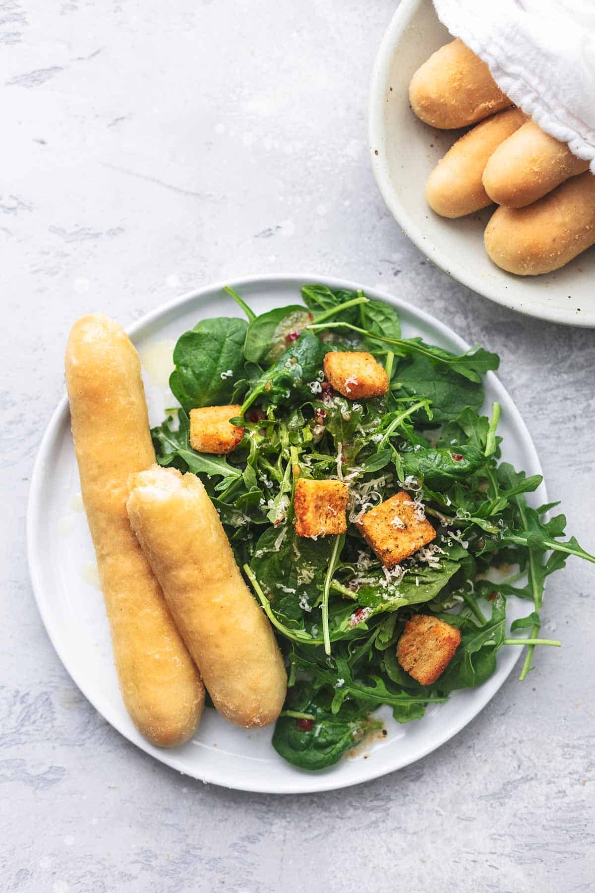 top view of Olive Garden breadsticks and salad on a plate with more breadsticks on a plate.