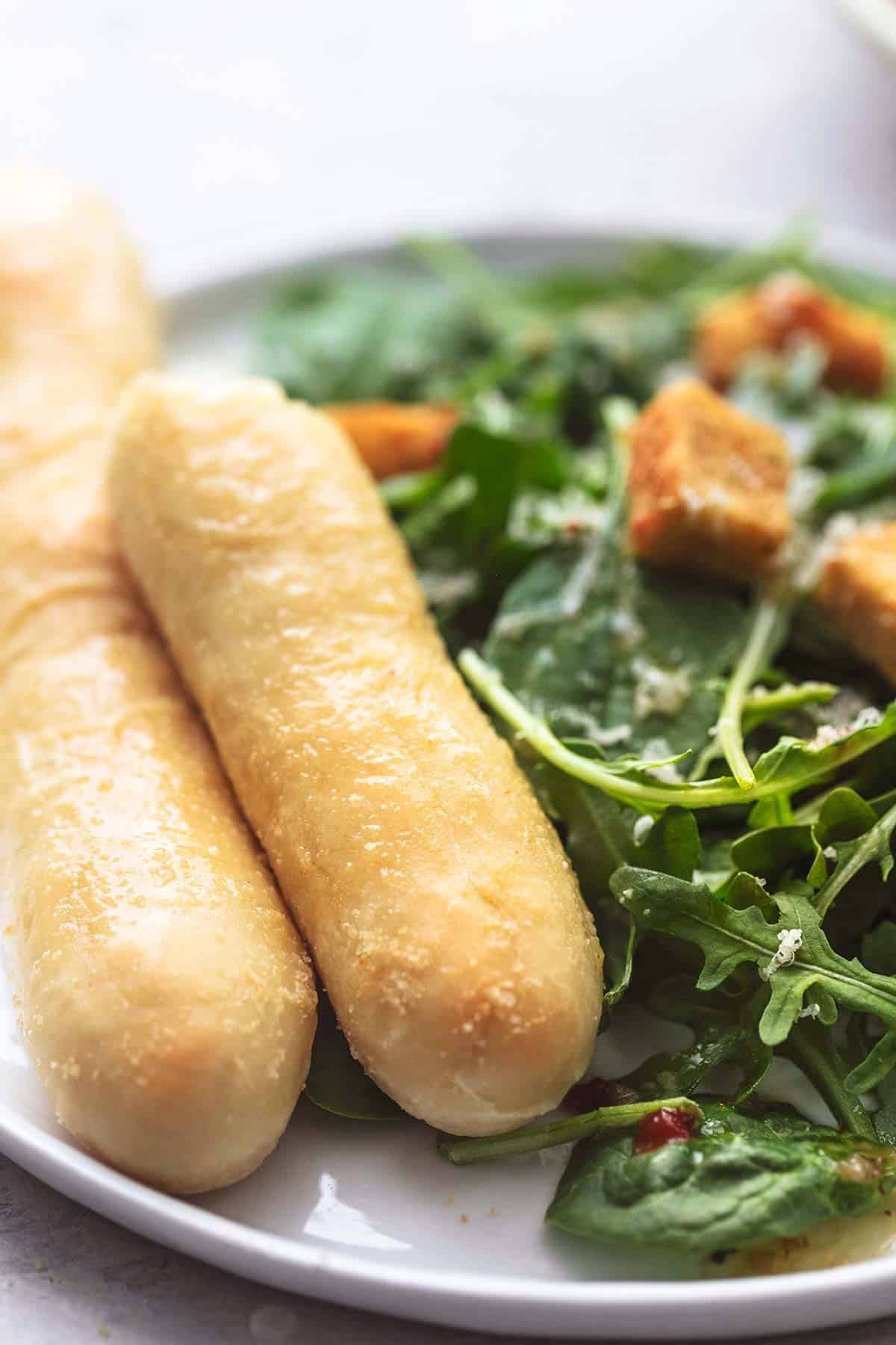 close up of Olive Garden breadsticks with salads on the side on a plate.