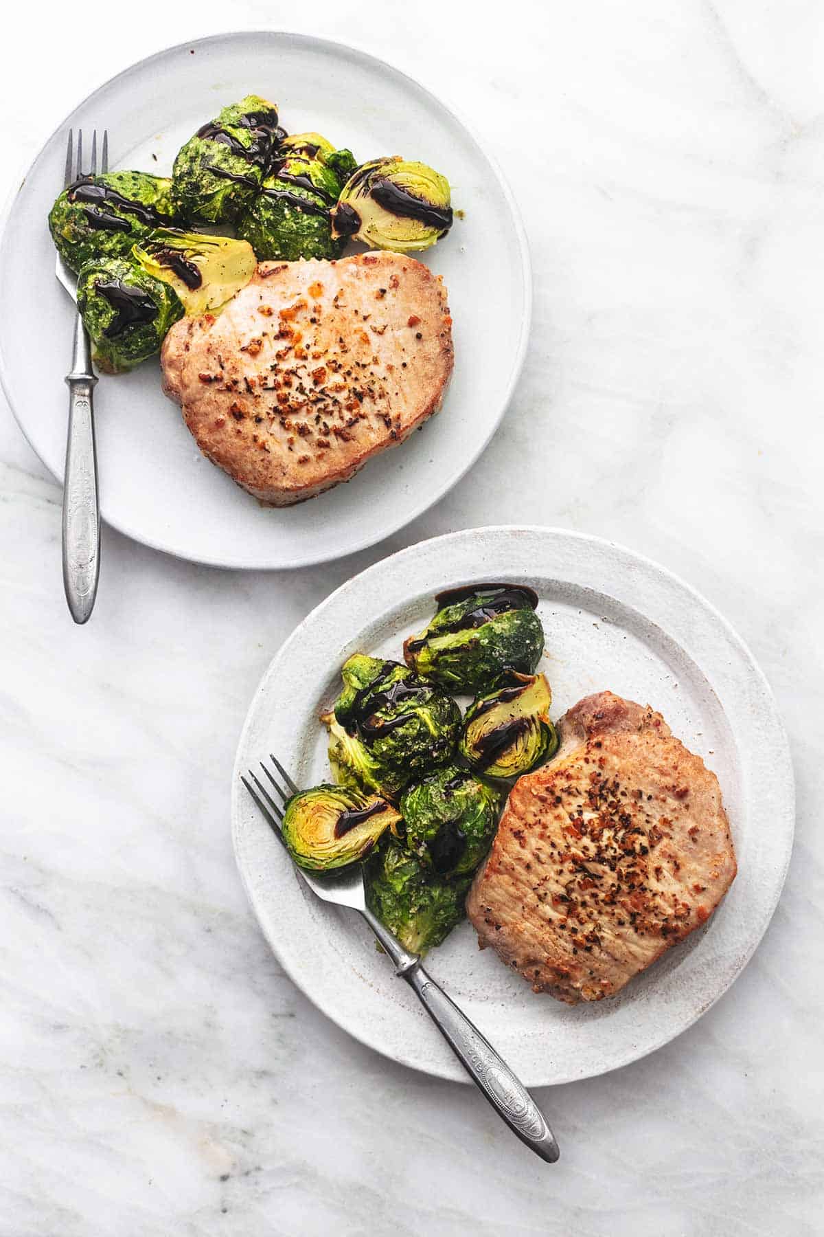 top view of two plates of pork chops and brussels sprouts with forks.