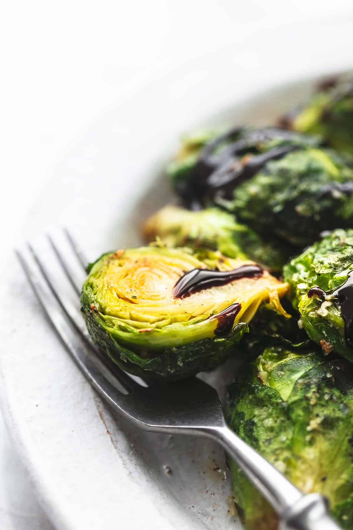 close up of brussels sprouts with balsamic with a fork on a plate.