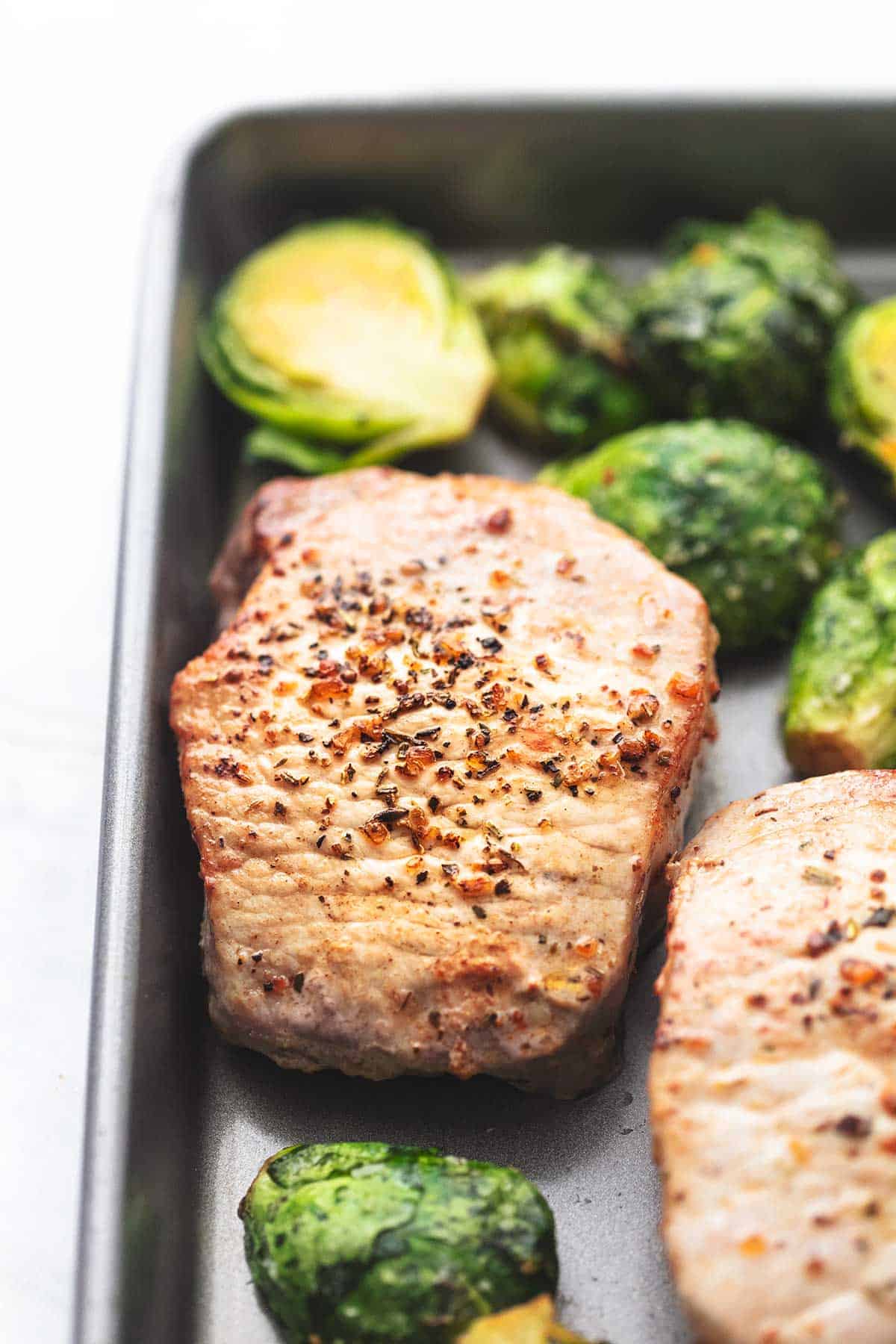 close up of pork chops and brussels sprouts on a baking sheet.