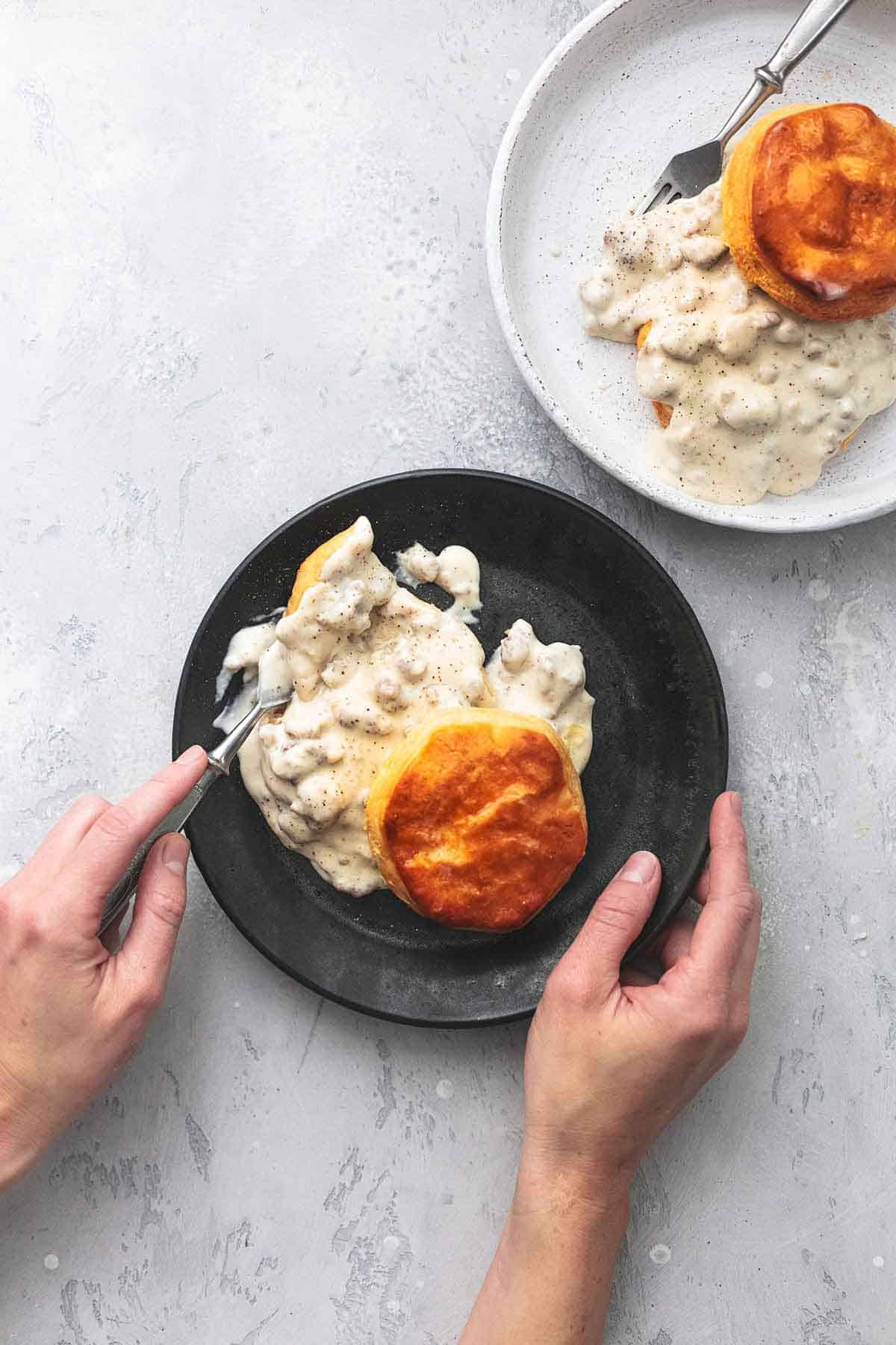 overhead hands holding fork and black plate with biscuits and gravy