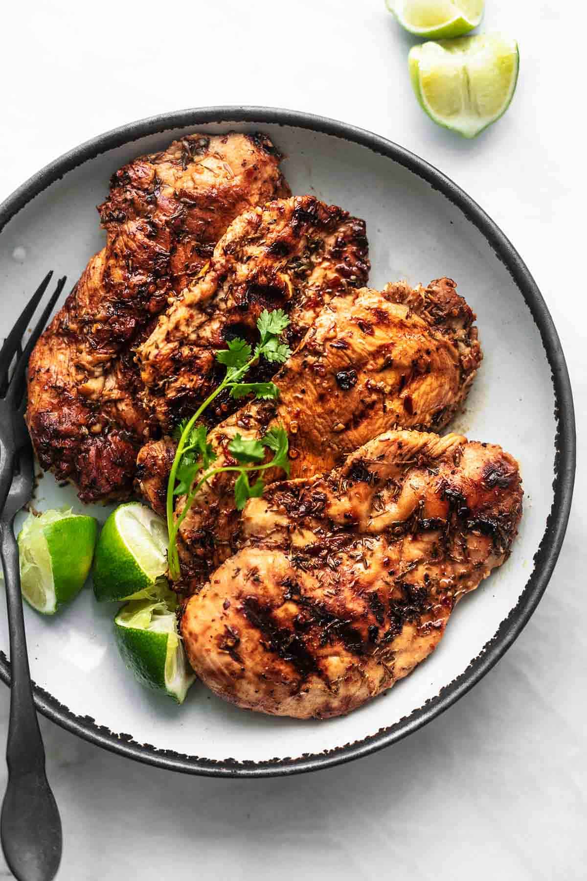 Caribbean jerk chicken with lime slices and a fork on a plate.