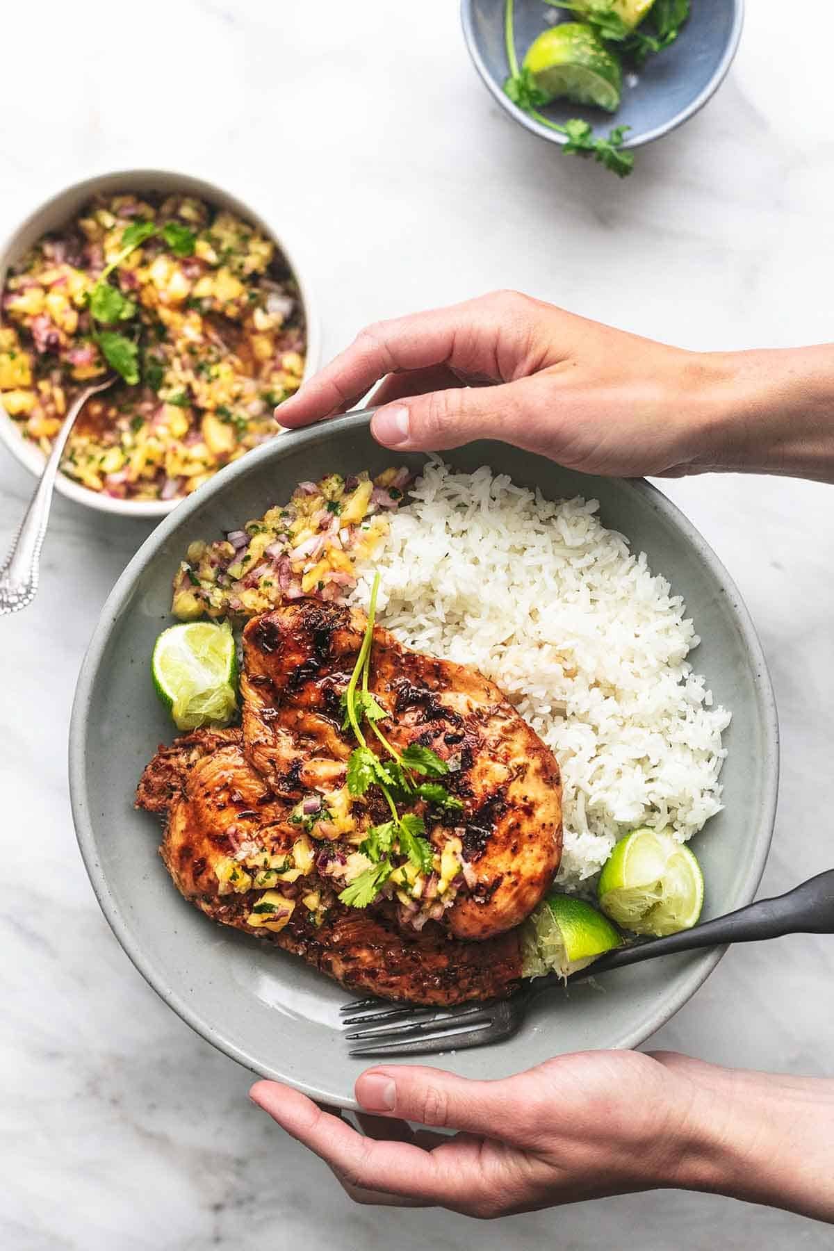 top view of hands holding a plate of Caribbean jerk chicken with pineapple salsa and rice with a fork on a plate.