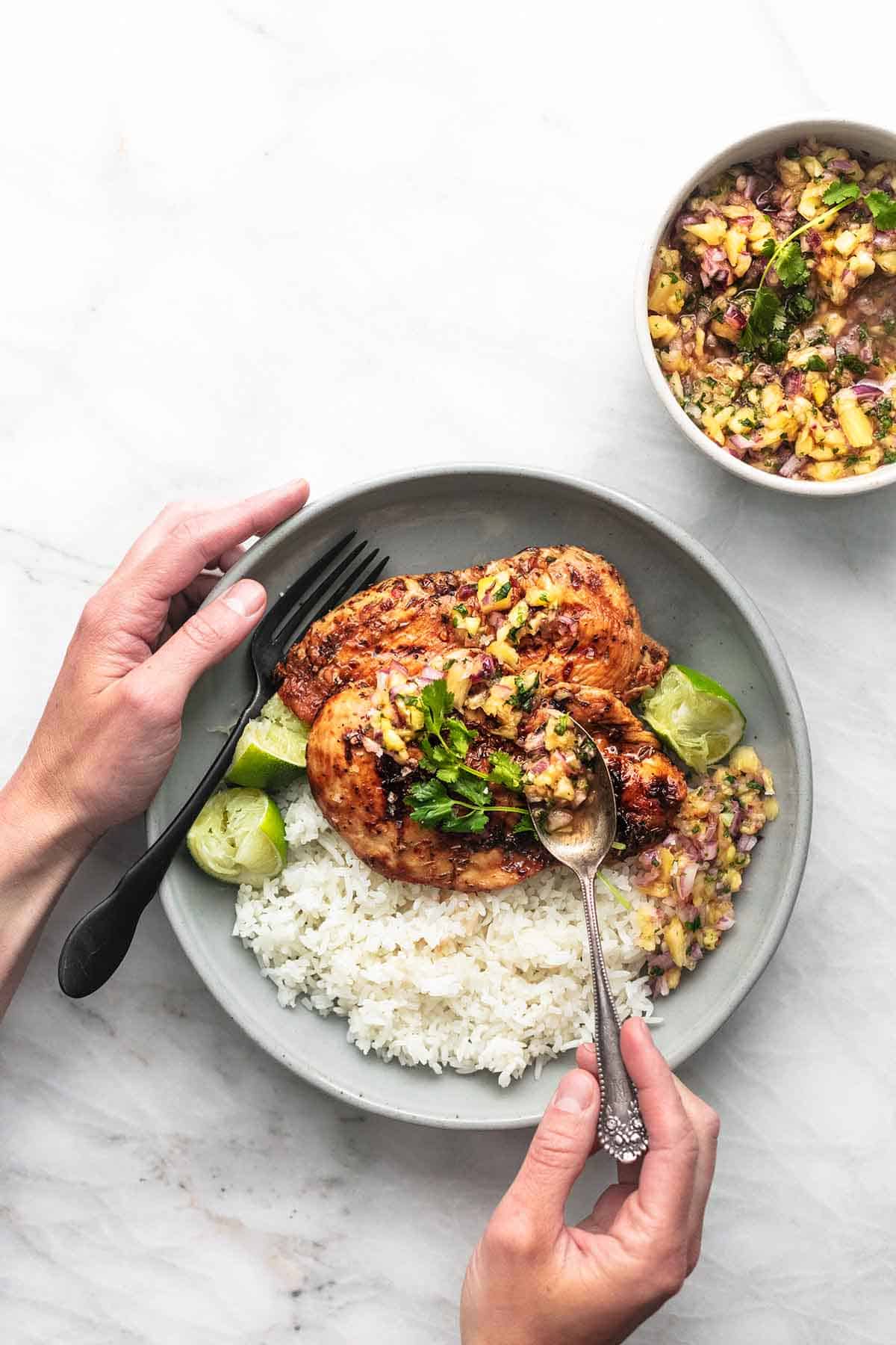 top view of a hand holding a plate of Caribbean jerk chicken with pineapple salsa and rice.