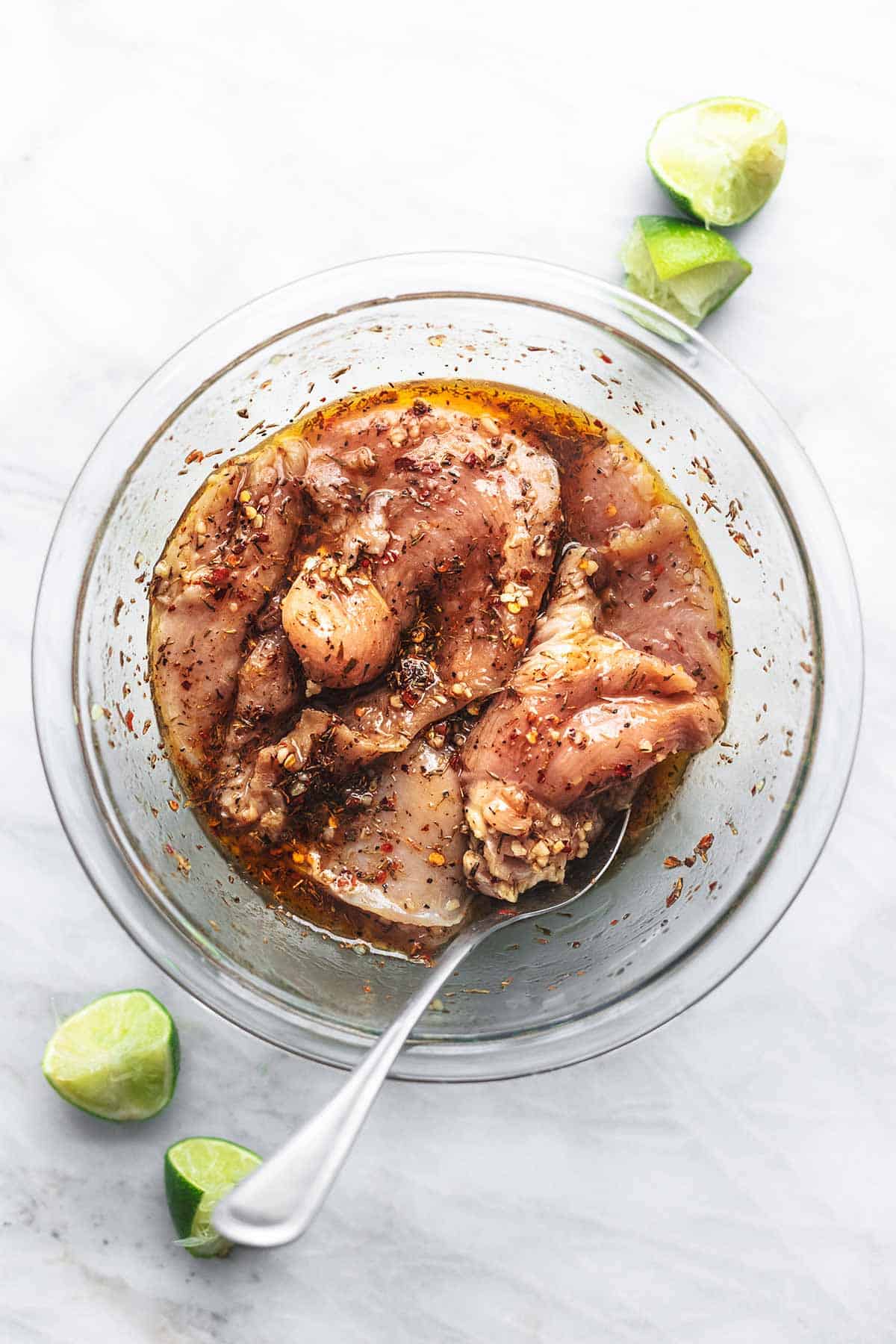 top view of raw chicken in marinade in a bowl with lime slices on the side.