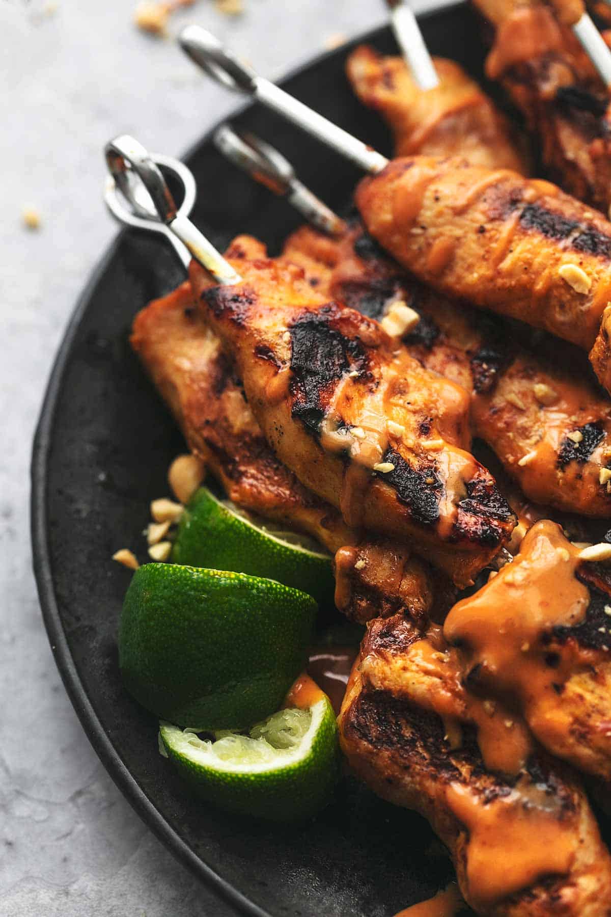 close up of chicken satay skewers with spicy peanut sauce and lime slices on a plate.