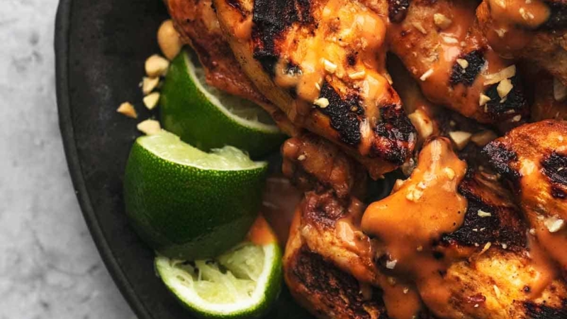 up close chicken satay skewers on plate with limes