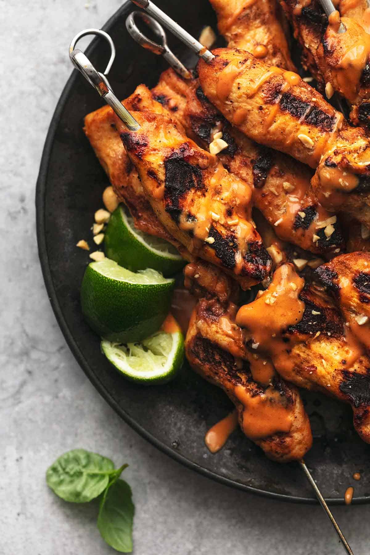 close up top view of chicken satay skewers with spicy peanut sauce with lime slices on a plate.