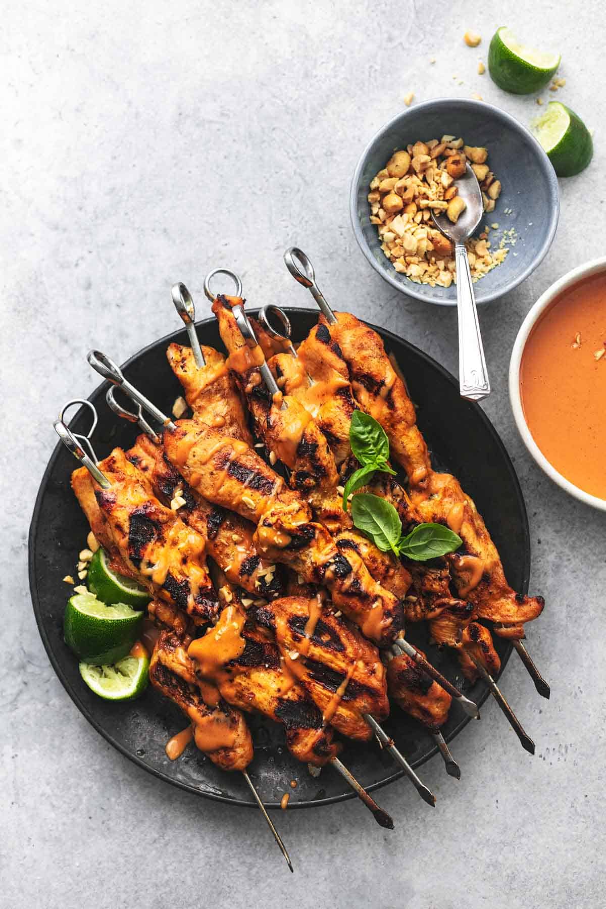 overhead chicken skewers on plate with limes and sauce and peanuts in bowls