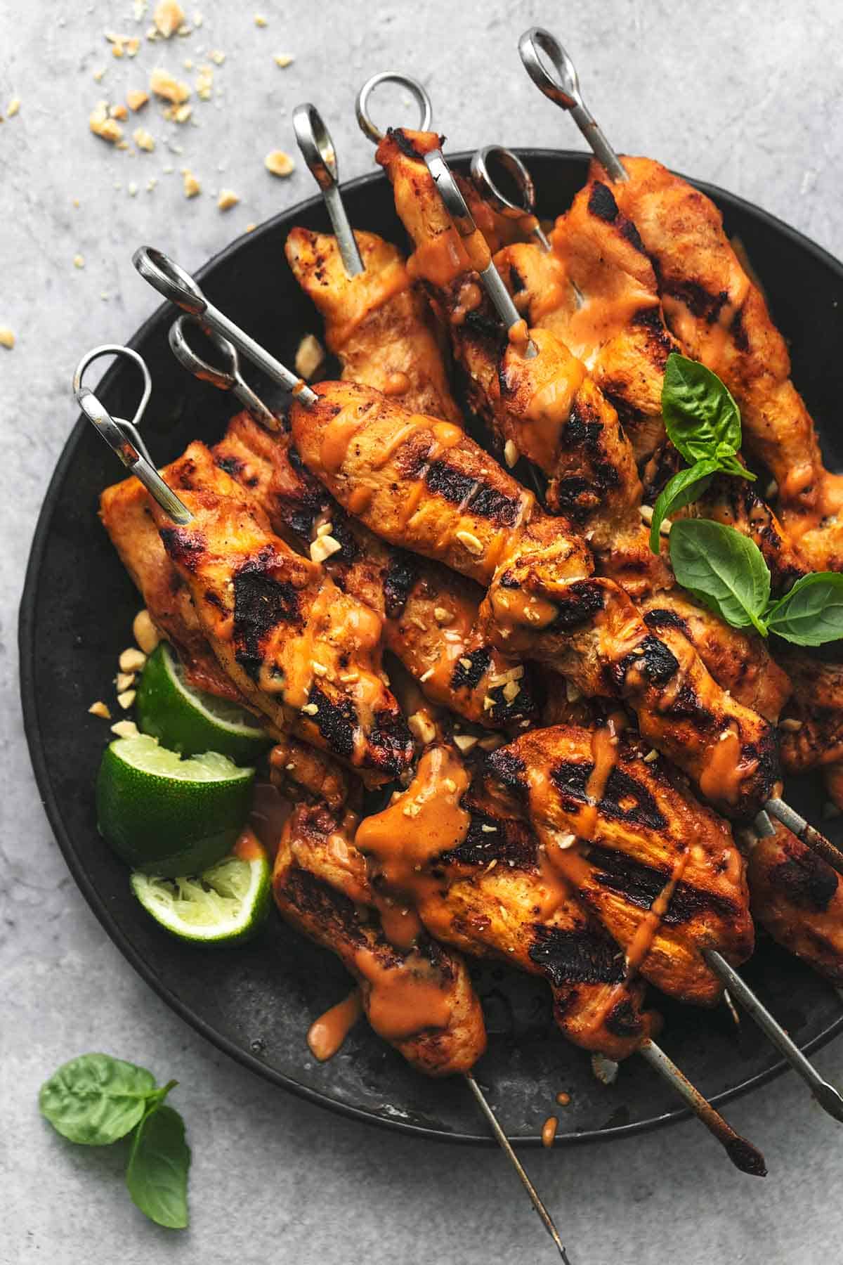 top view of chicken satay skewers with spicy peanut sauce with lime slices on a black plate.