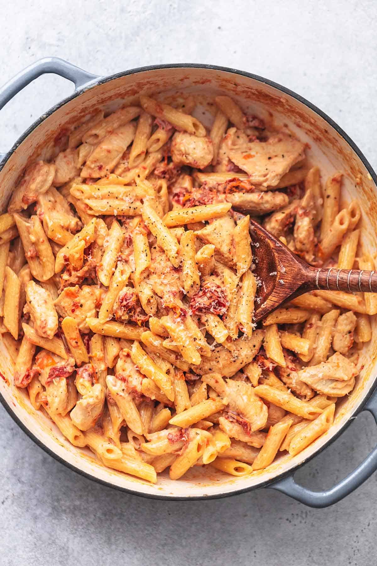 top view of creamy sun-dried tomato chicken pasta with a serving spoon in a skillet.