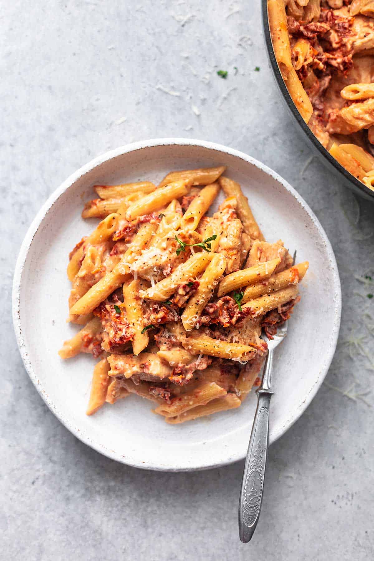 top view of creamy sun-dried tomato chicken pasta on a white plate with a fork.